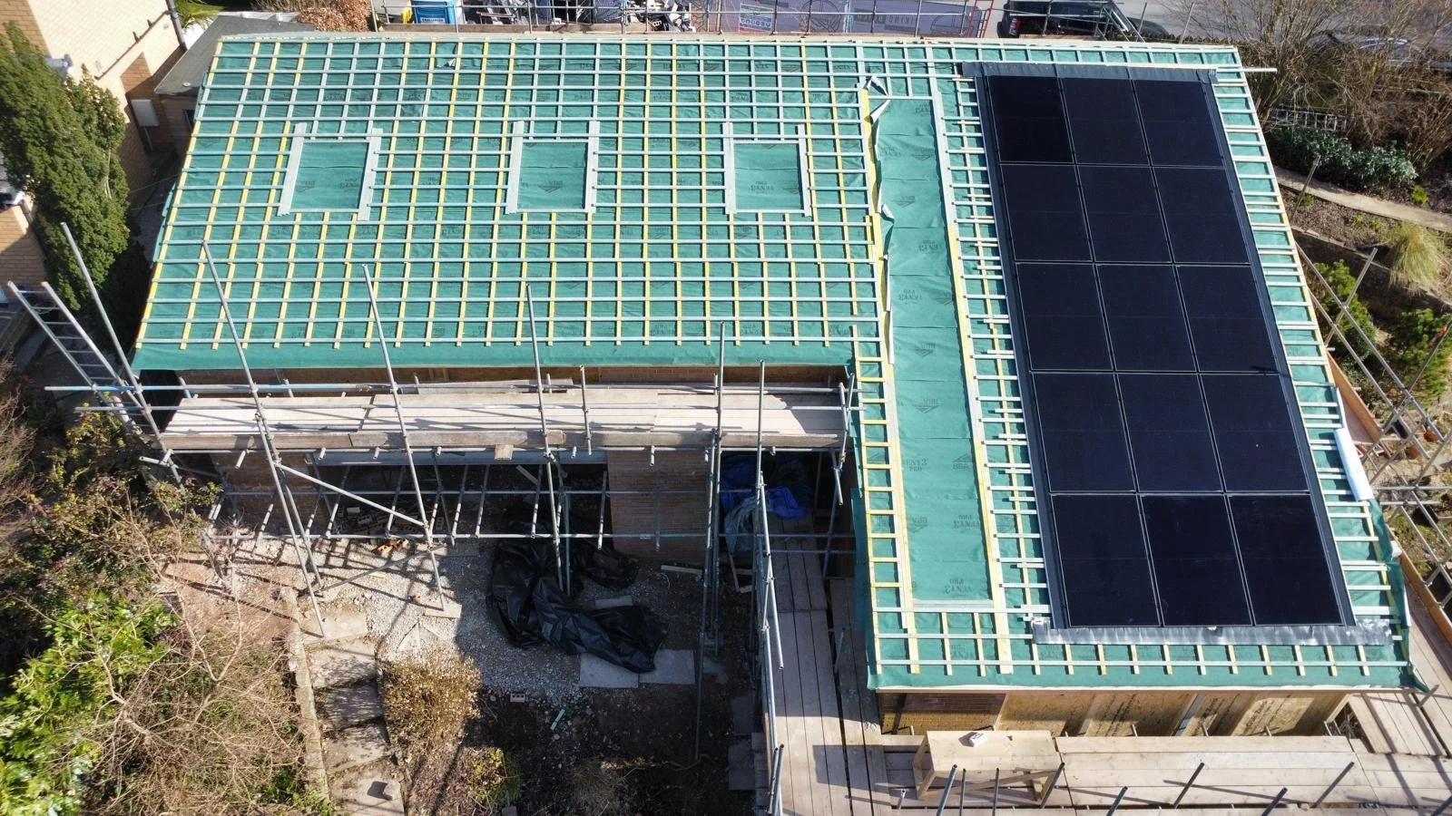 Aerial view of a house under construction with solar panels installed on the roof and scaffolding around it.