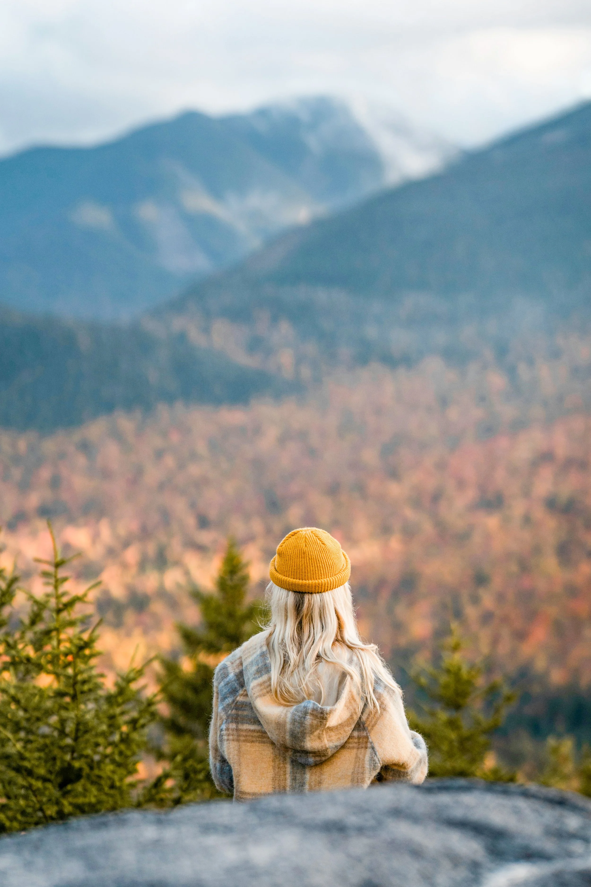 Anonymous photographer with yellow hat looks out over mountains in autumn