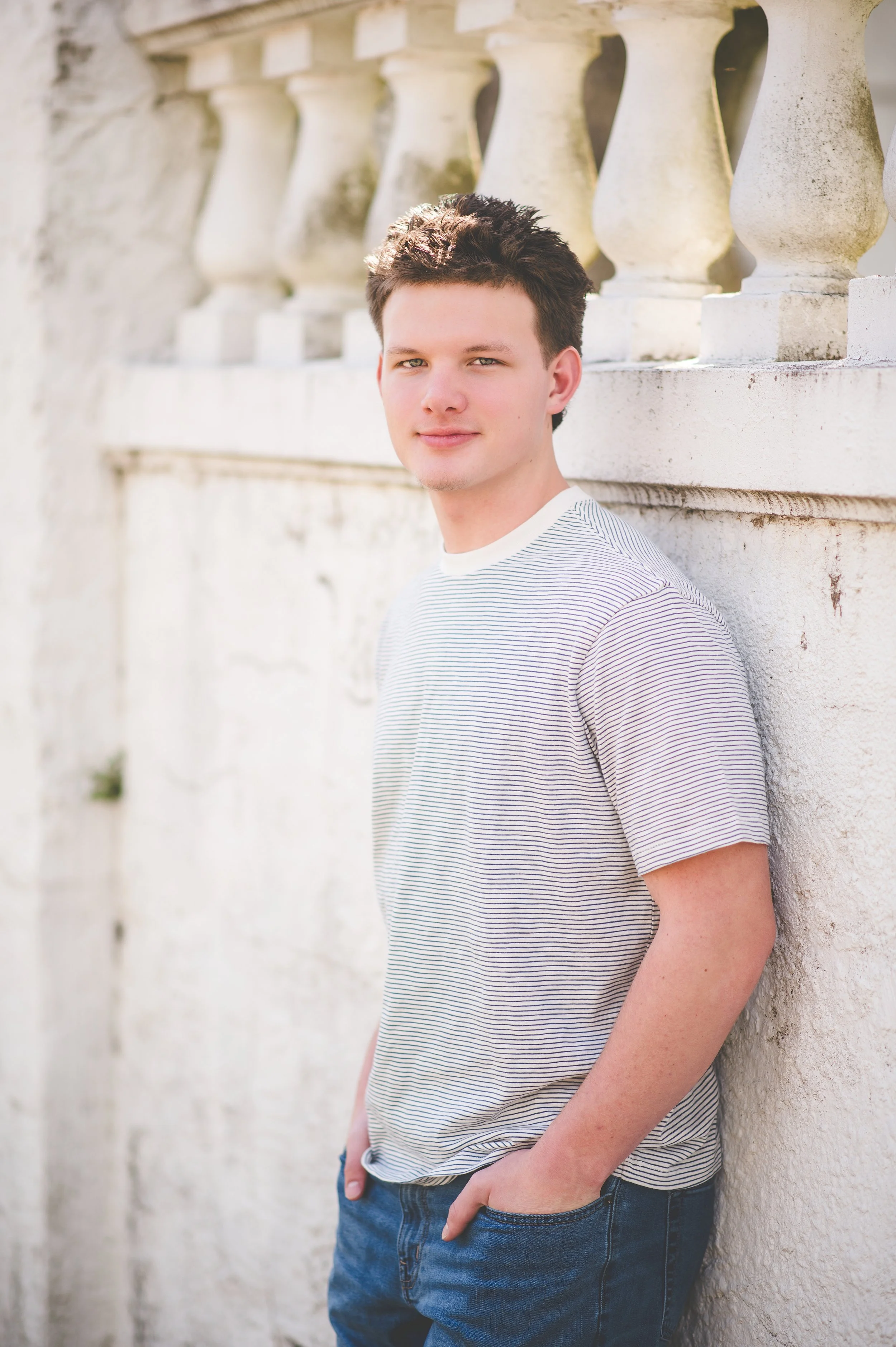 Young man squatting on gravel near train tracks with a wooden building in the background, during sunset.