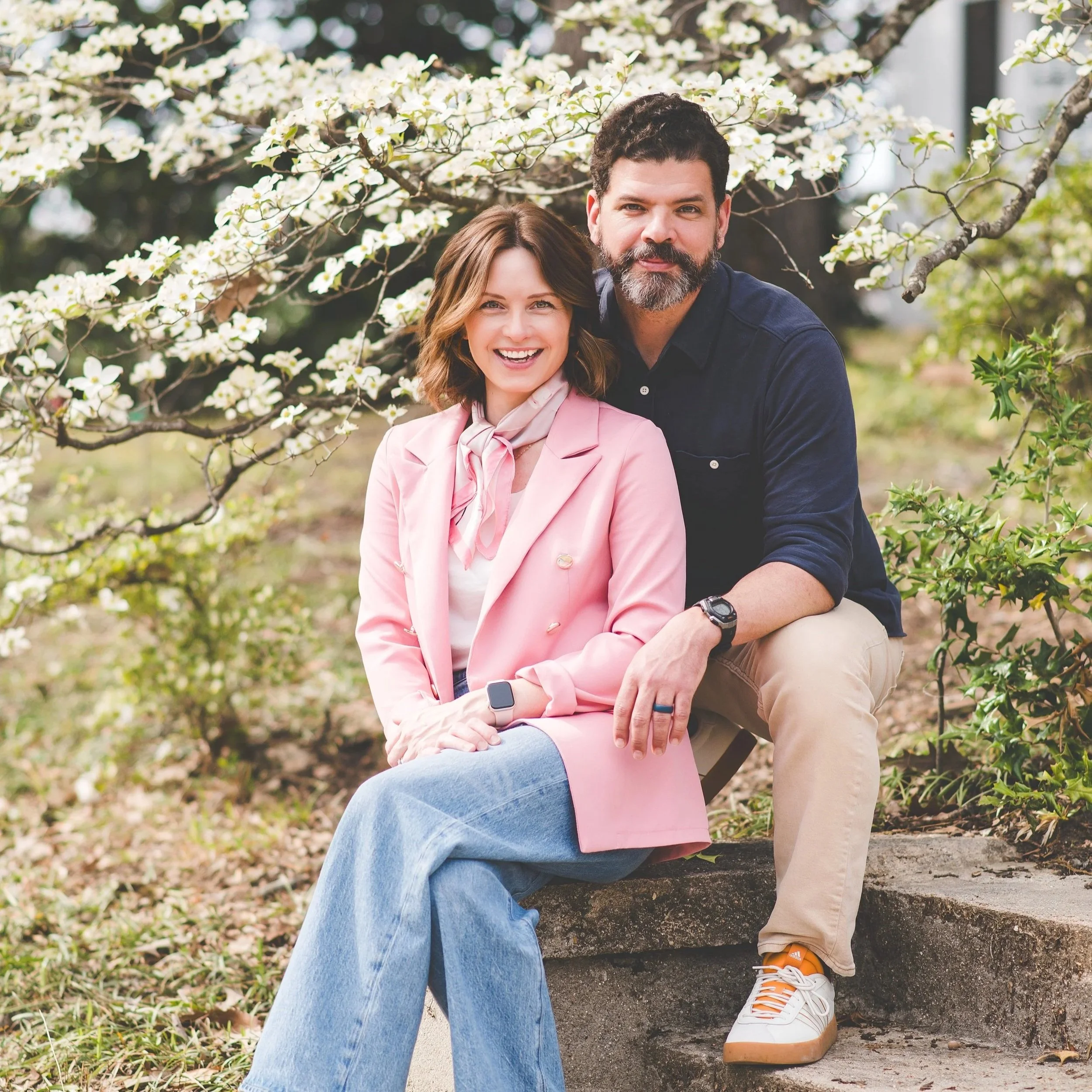 A couple smiling and hugging outdoors near a railway track during sunset.