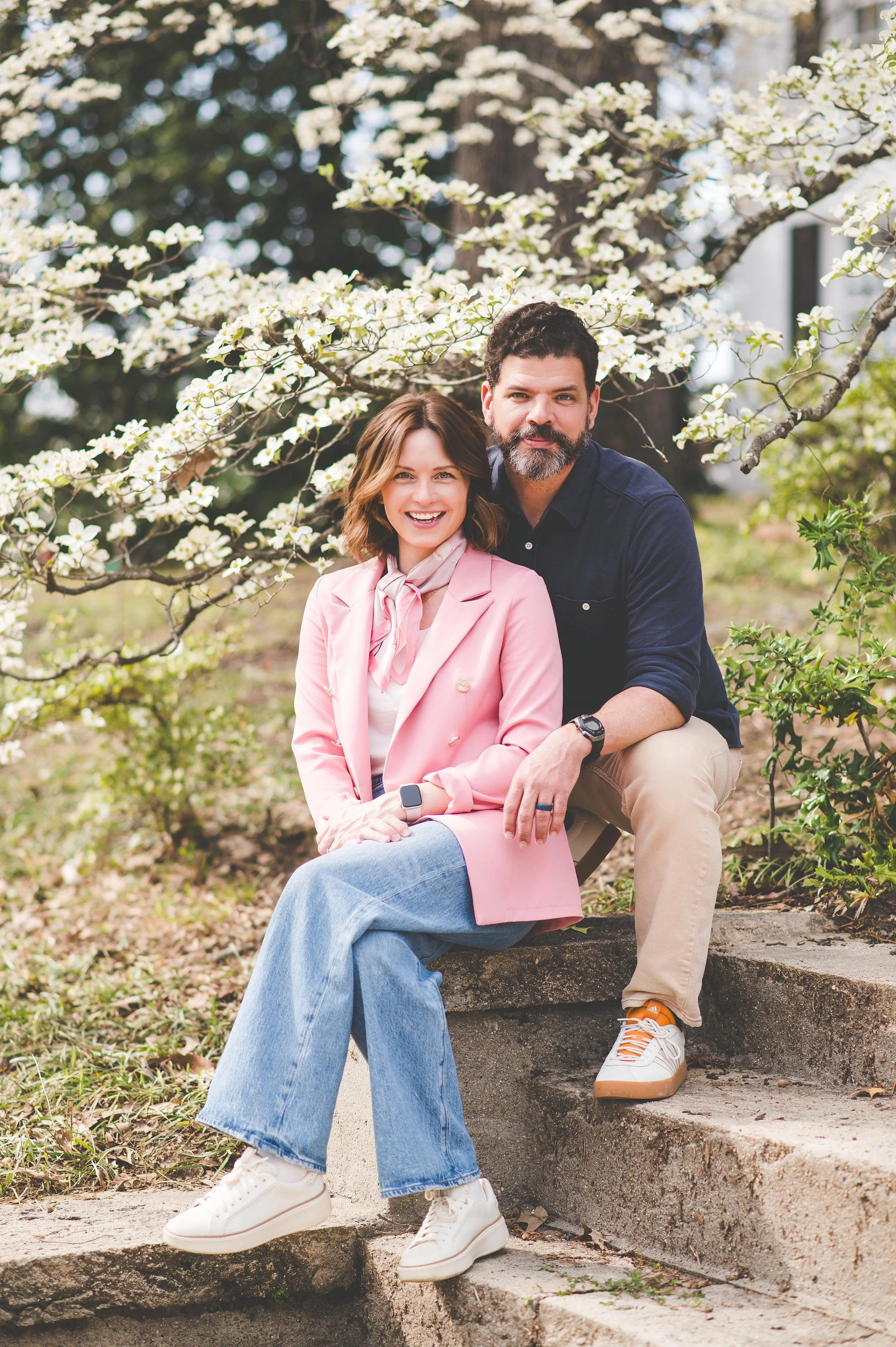 A couple smiling and hugging outdoors near a railway track during sunset.