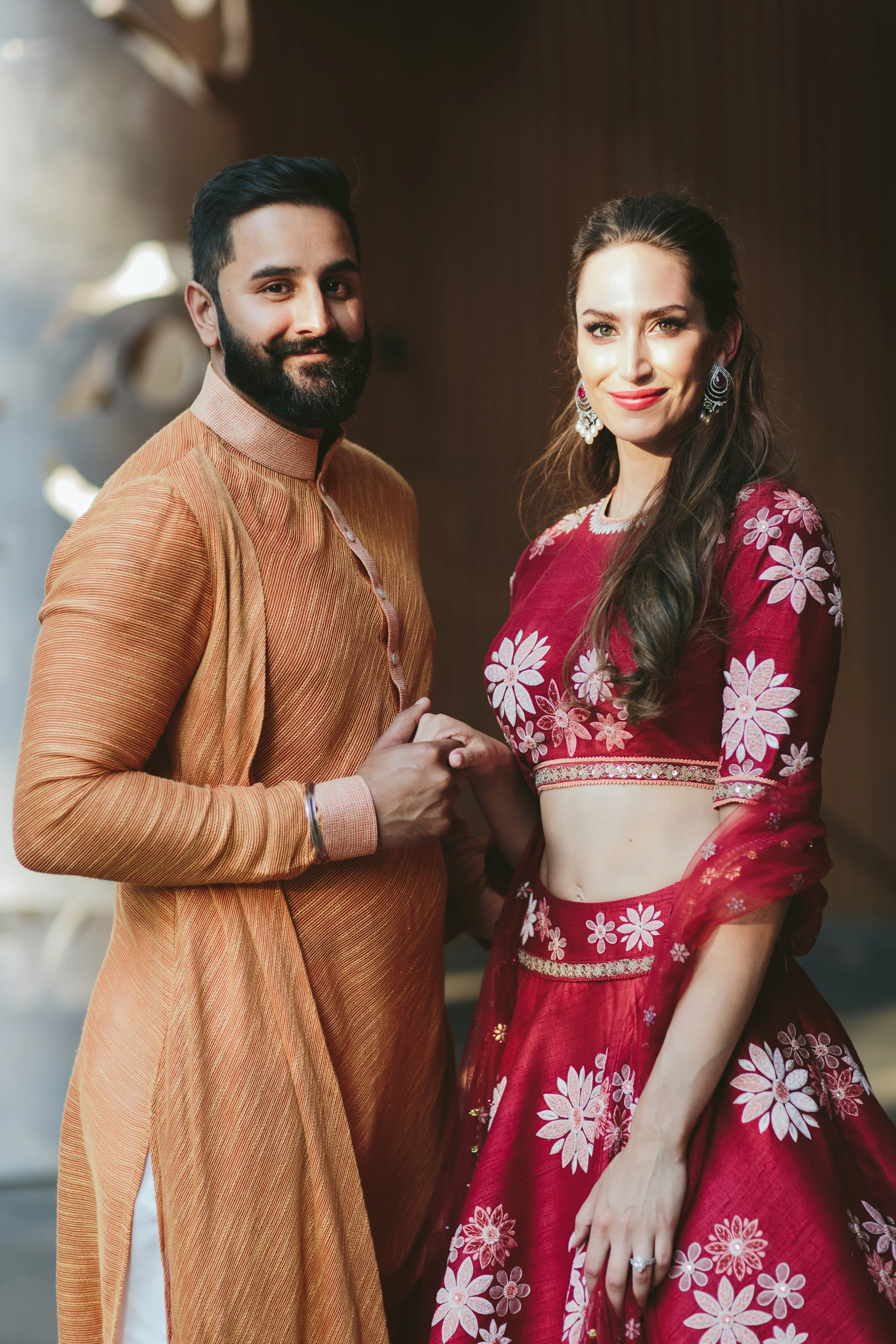 A man and woman dressed in traditional Indian attire holding hands and posing for the camera.