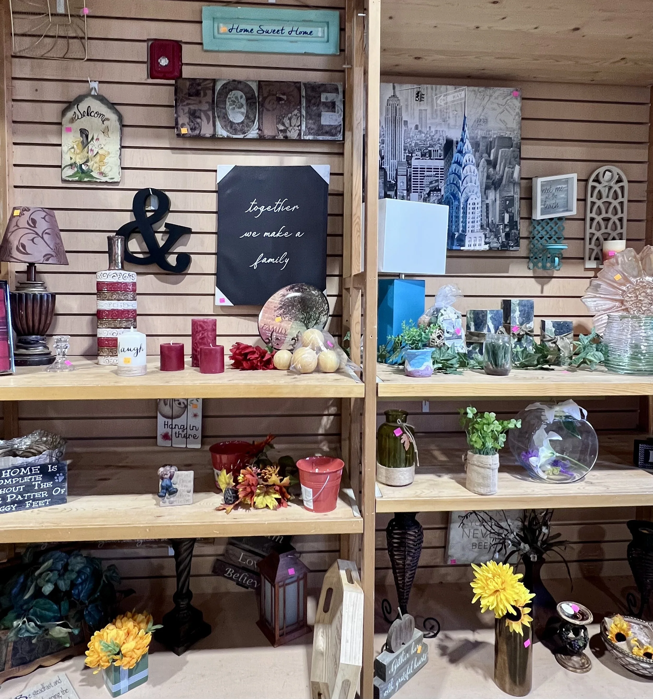 Display of decorative home and wall decor items including framed signs, flower arrangements, and figurines on wooden shelves.