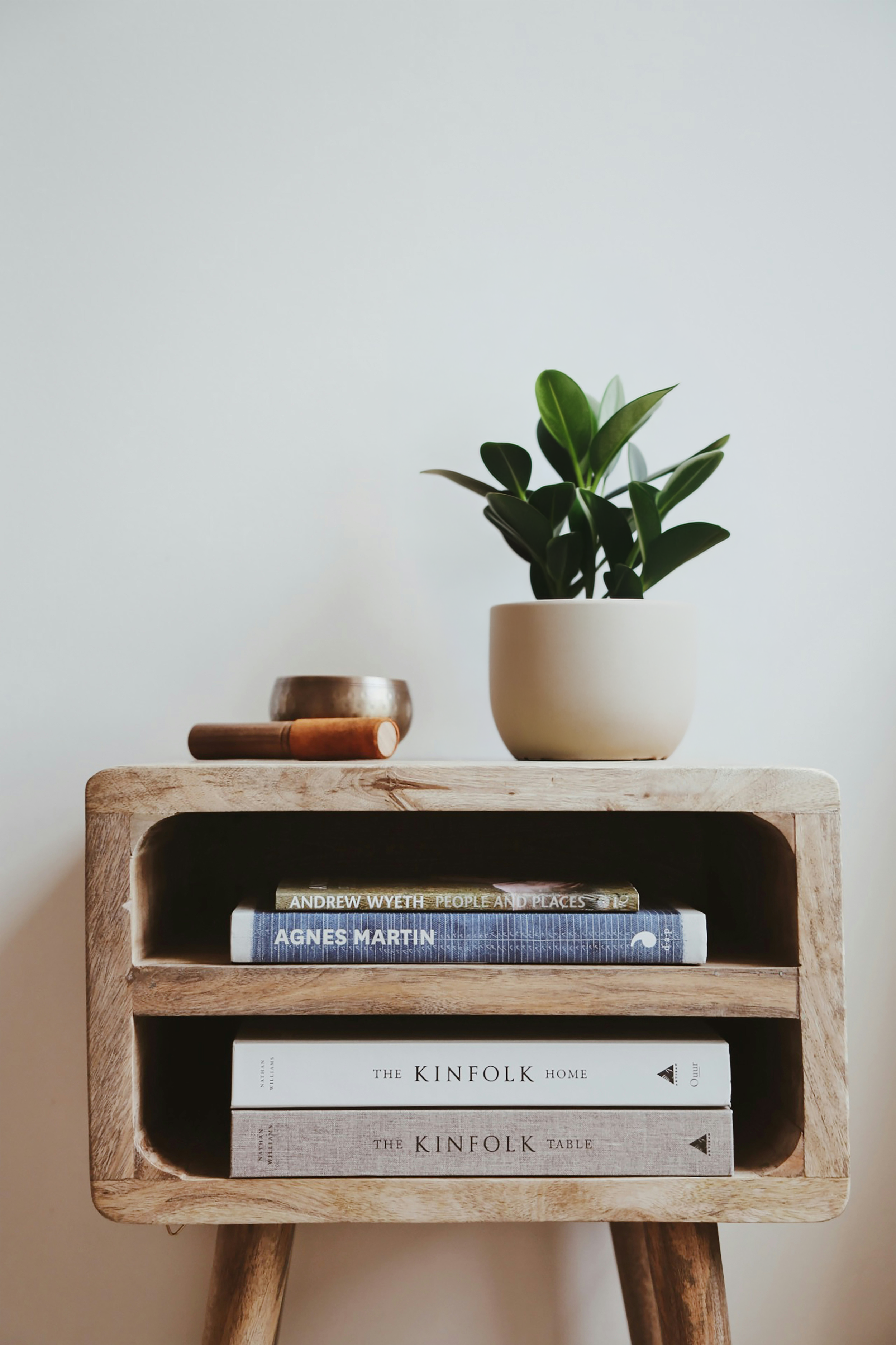 A wooden side table with a potted plant, decorative objects, and books on it, against a light-colored wall.