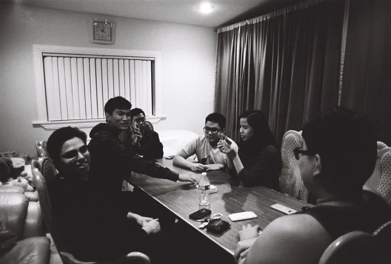 Past friends sitting around the table playing Exploding Kittens, a card game.
