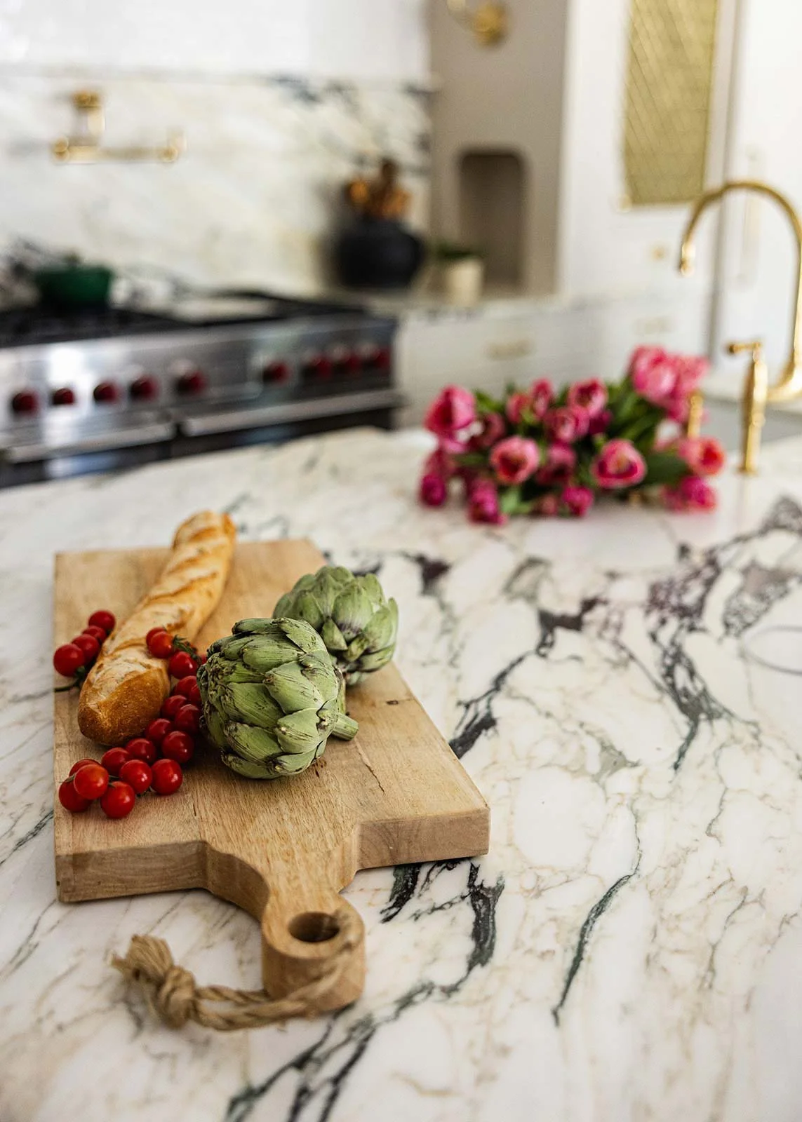 Beautiful marble kitchen island with a cutting board hosting bread, berries, and artichokes