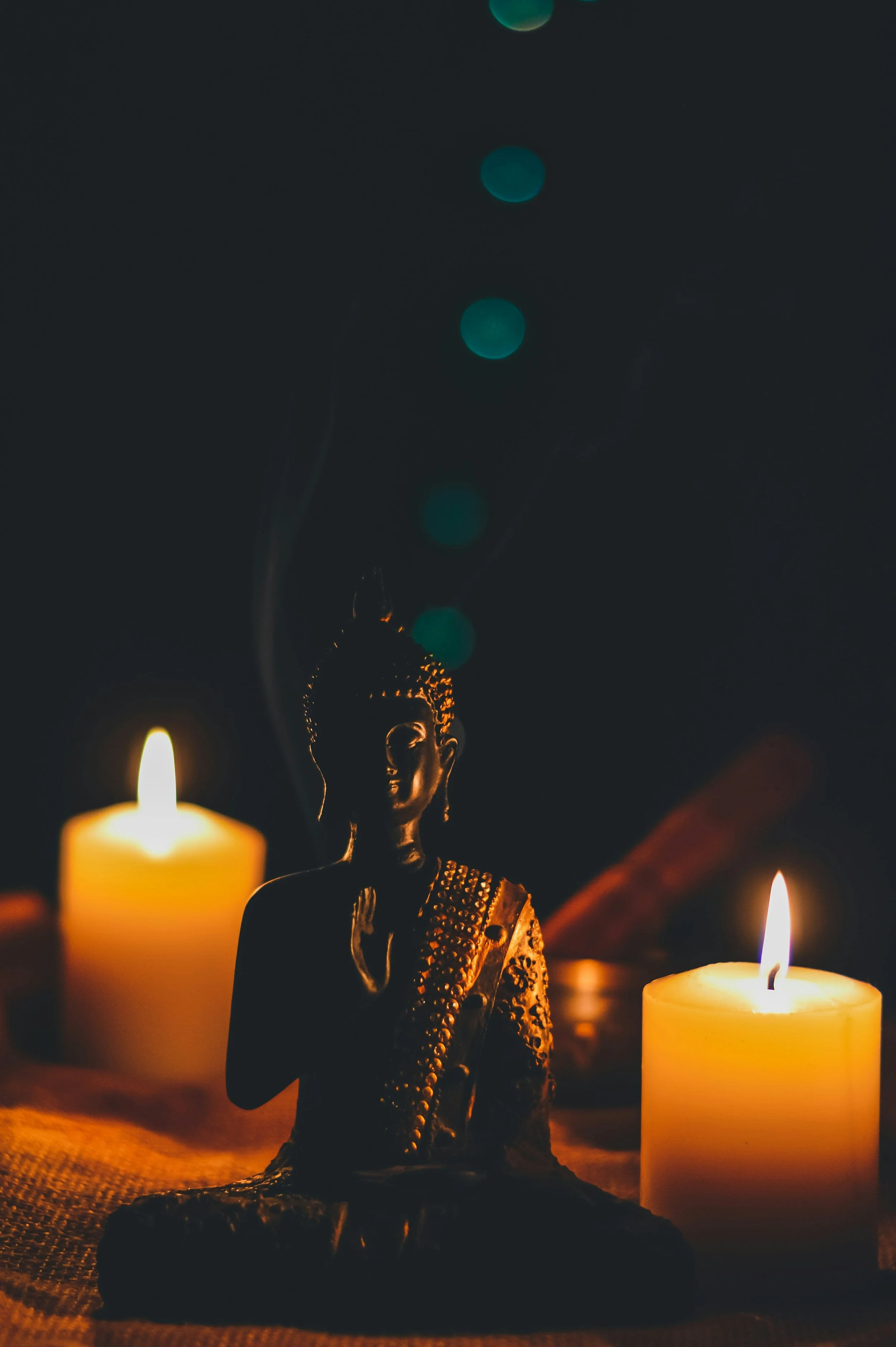 A Buddha statue illuminated by two lit candles in a dark setting.