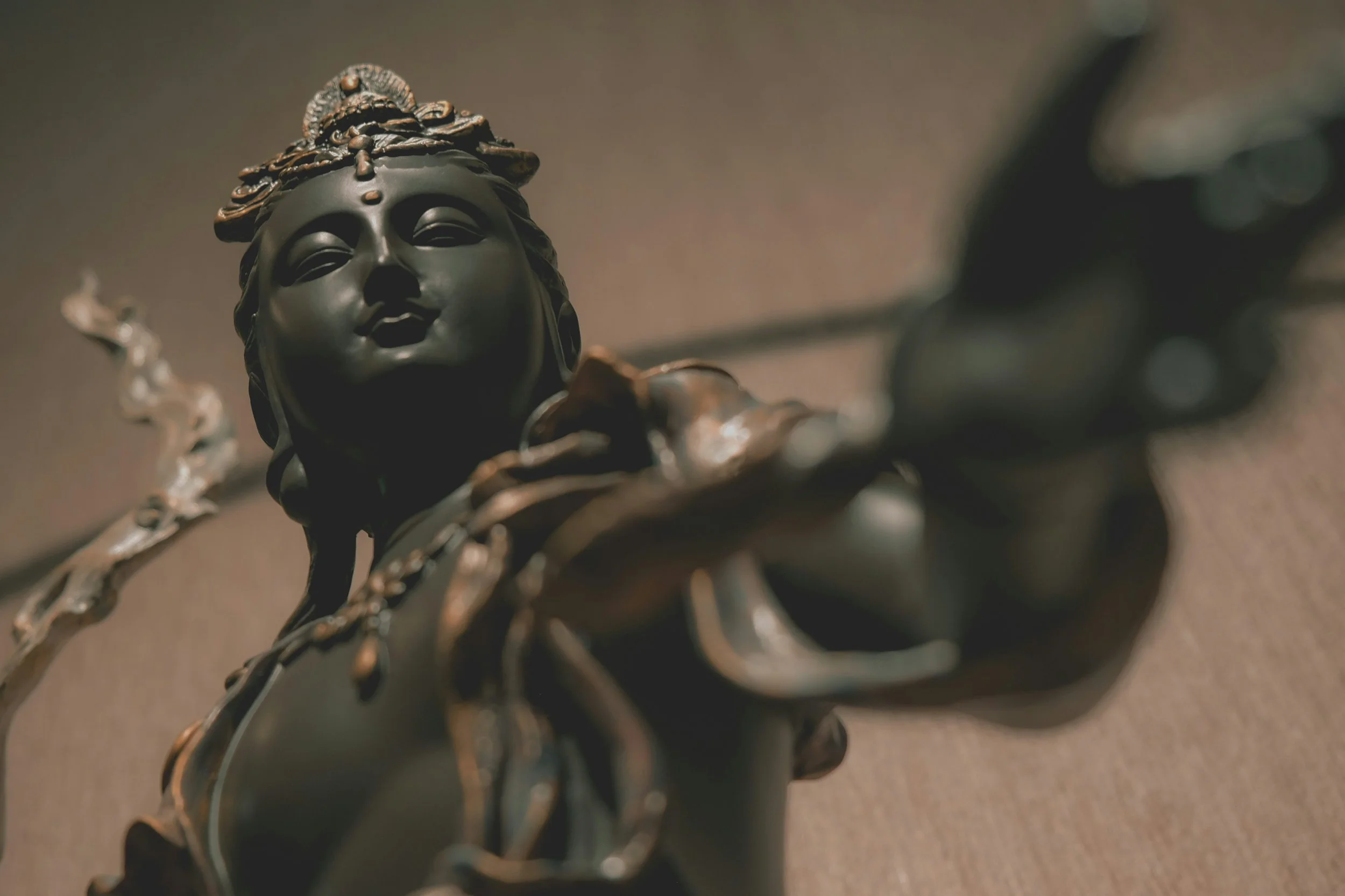 Close-up of a dark-colored sculpture of a woman's face with detailed hair and earrings, set against a plain background.