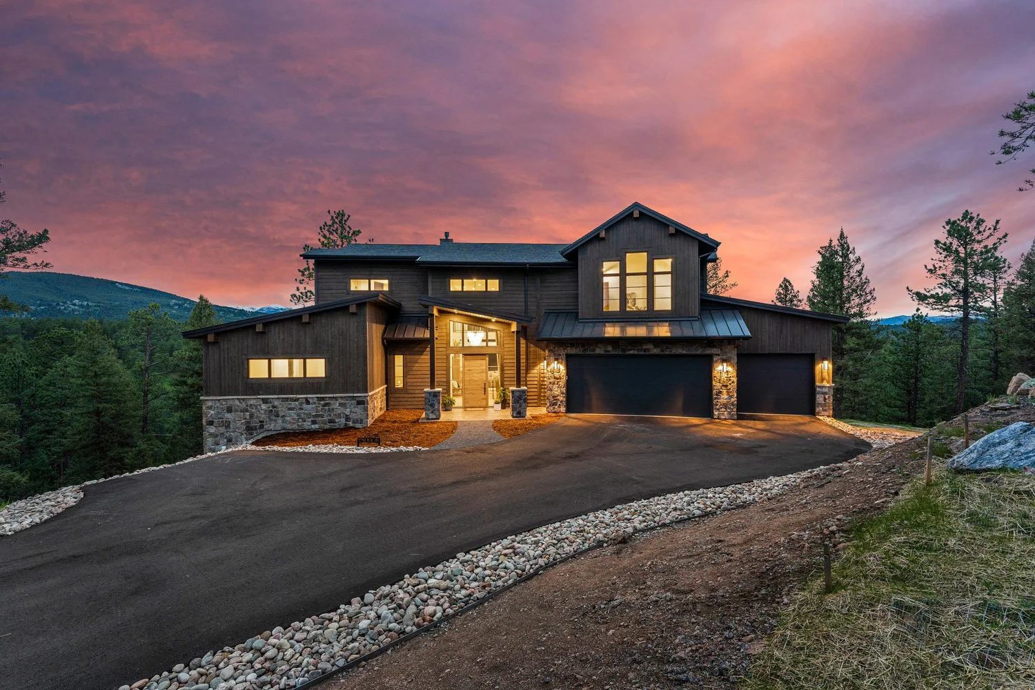 Modern rustic house surrounded by trees with a sunset sky designed by LGA Studios for a custom hillside build in Colorado.
