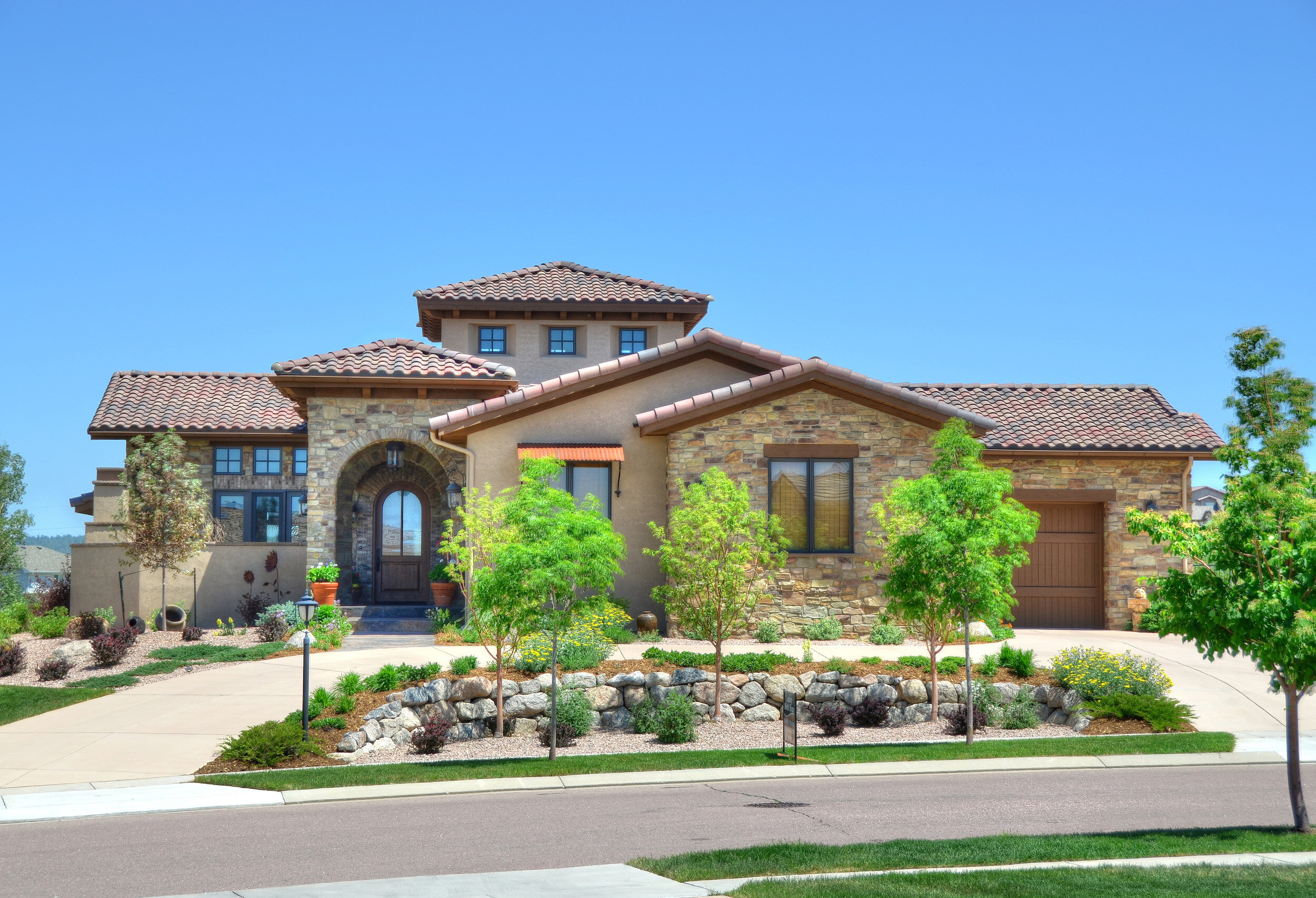 Exterior of a modern Tuscan house with a tiled roof, large windows, and stone accents. Sustainable home design in Colorado Springs by LGA Studios.