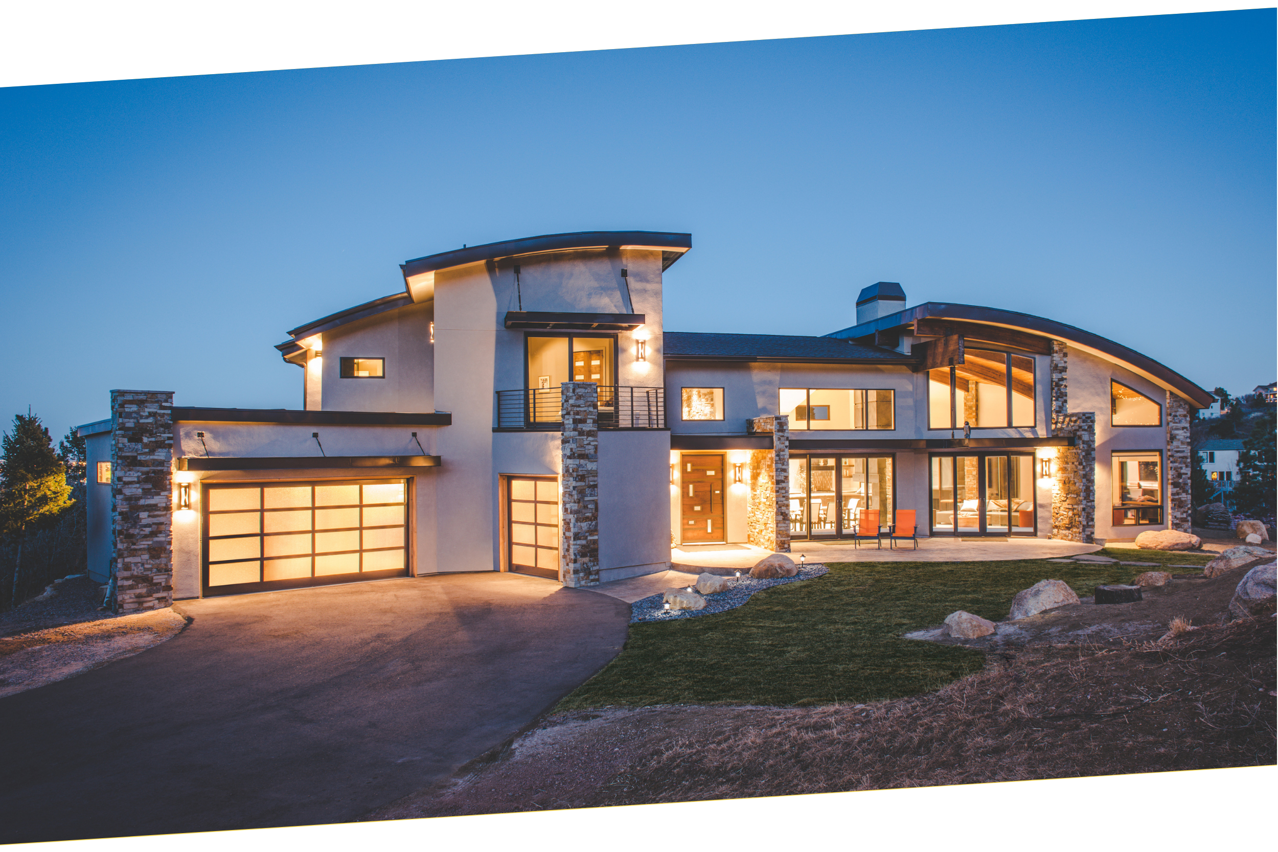 Contemporary luxury house with large windows and stone accents, illuminated at dusk. Custom home designed by LGA Studios in Colorado Springs.