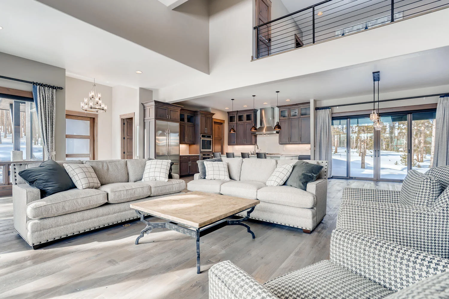 Modern open-concept living room and kitchen with a large window view of a snowy mountain landscape. Custom hillside home designed by LGA Studios.