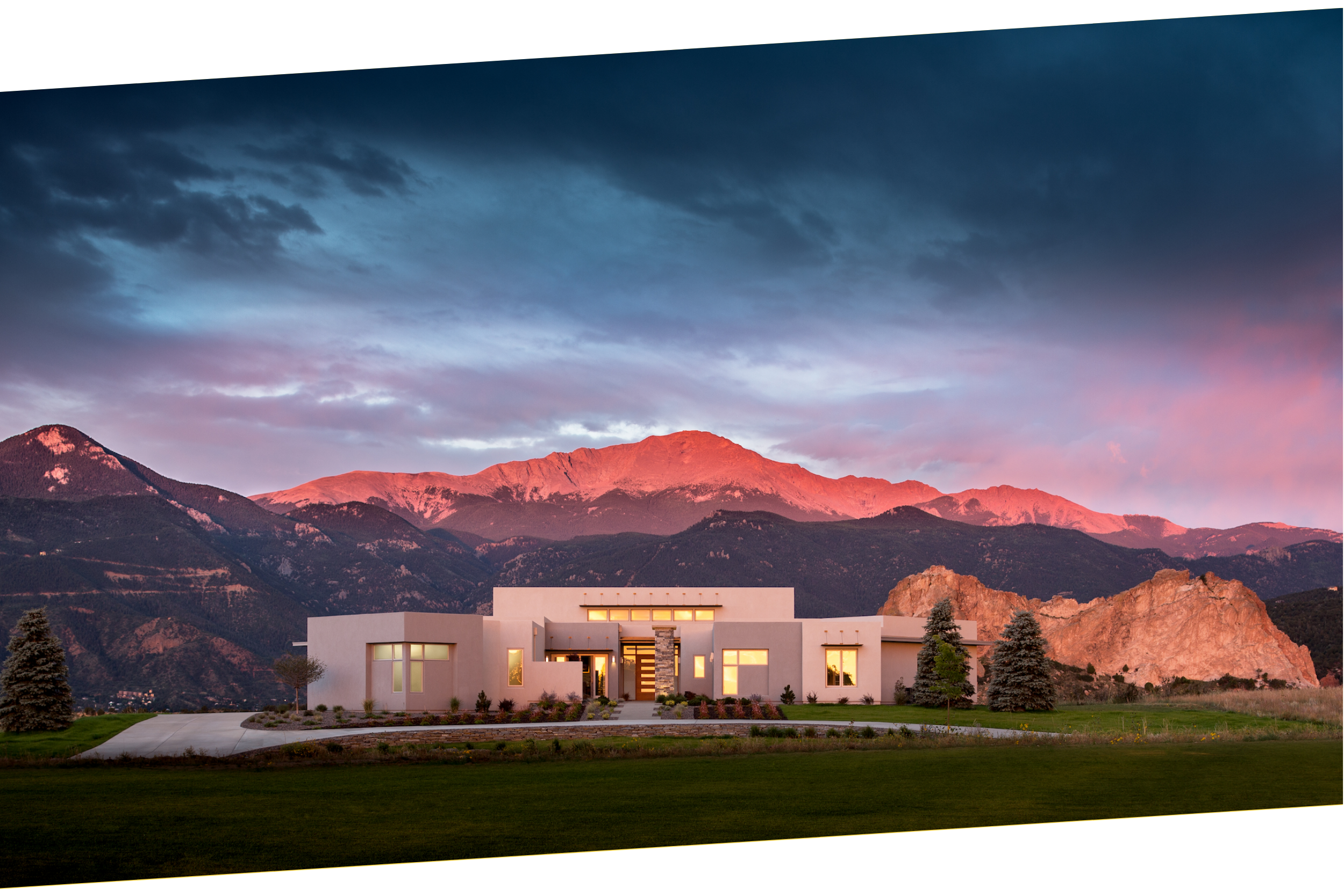 Modern custom house designed by LGA Studios in front of Rocky Mountains at sunset, with a dramatic sky and illuminated mountain peaks. Minimalist luxury home in Kissing Camels, Colorado Springs. 