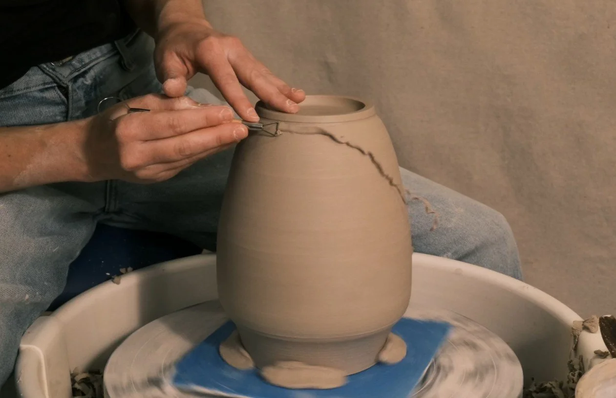 Artist, Ada Dolan, working on a large ceramic vase on a pottery wheel, trimming the foot of a vase.