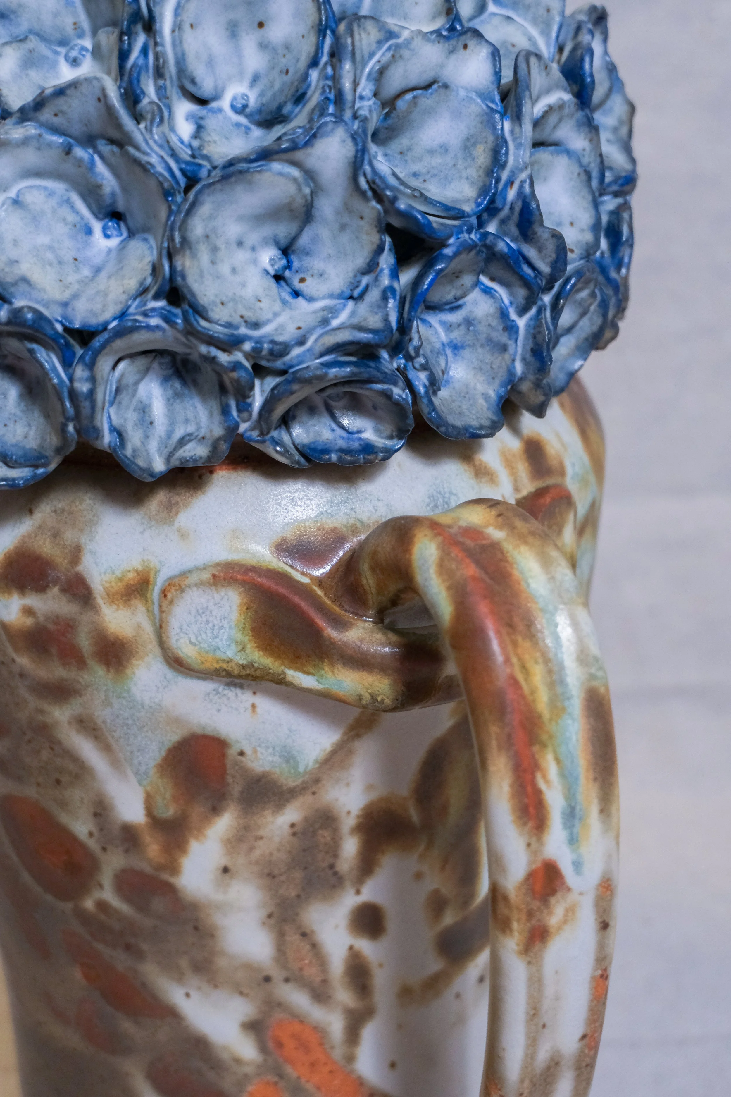 Close-up of a ceramic sculpture with blue and white hydrangea lid and a base with brown white, and blue abstract patterns.