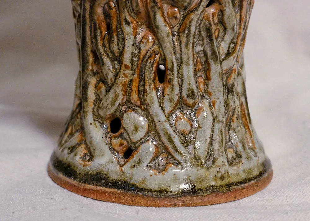 Close-up of the bottom of a ceramic vase with a green and brown, textured, vine like pattern.