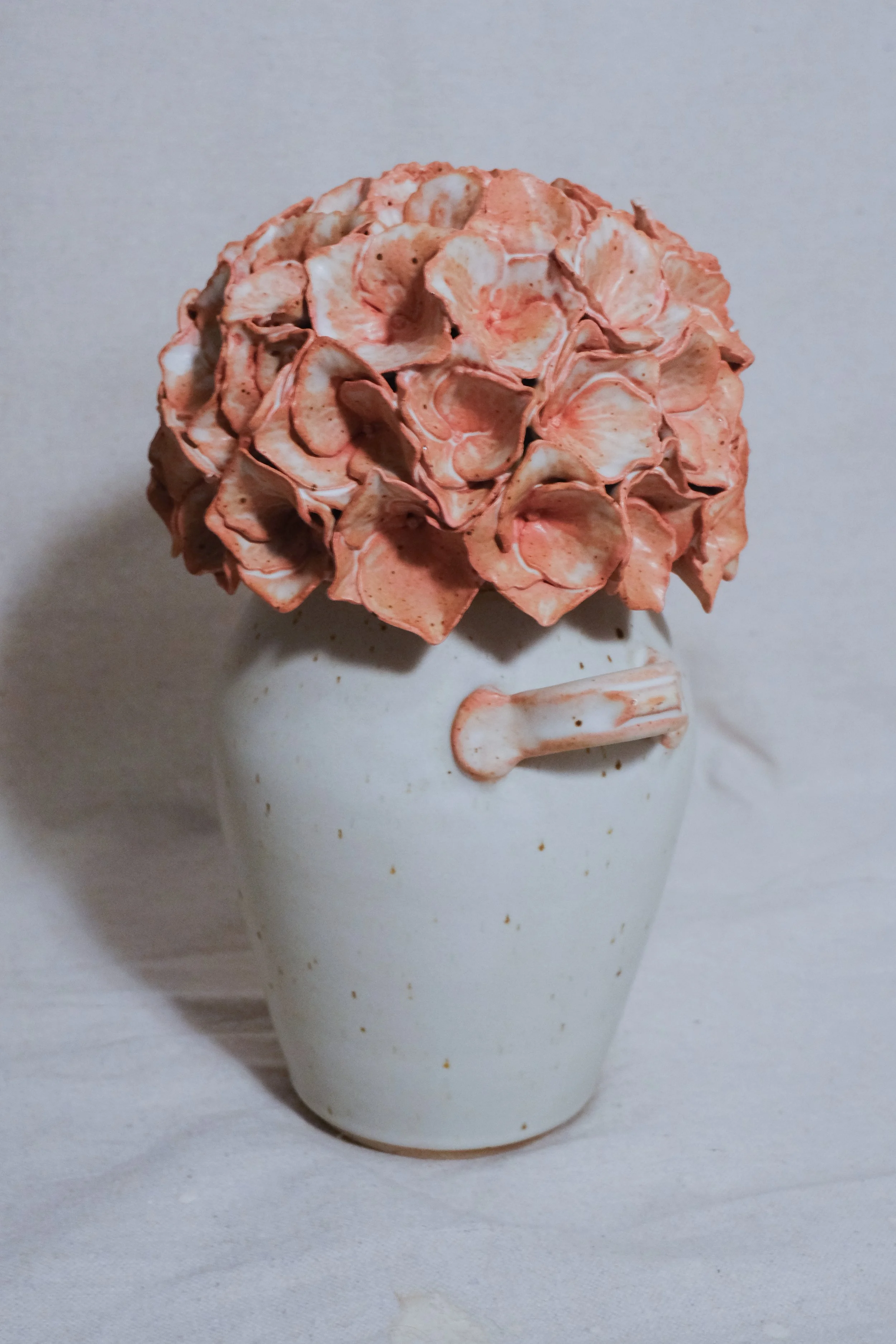 A white ceramic vase filled with a pink and white handle, and the lid is a dusty pink sculpted hydrangea