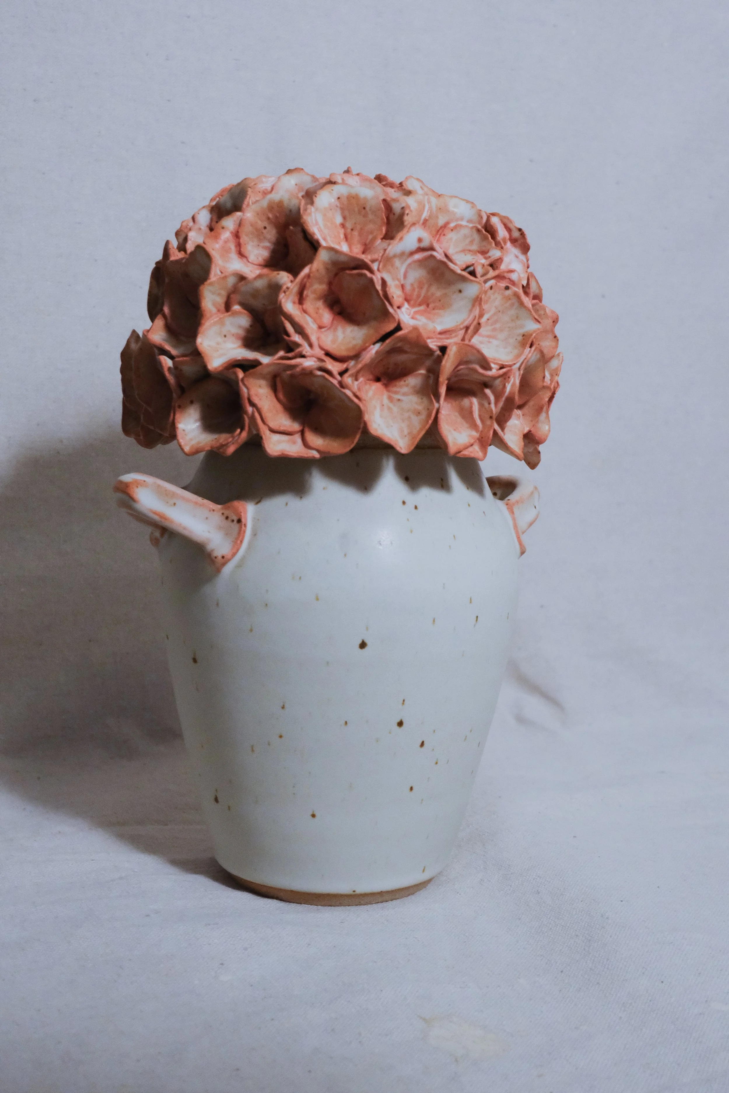 A white ceramic vase filled with a pink and white handle, and the lid is a dusty pink sculpted hydrangea