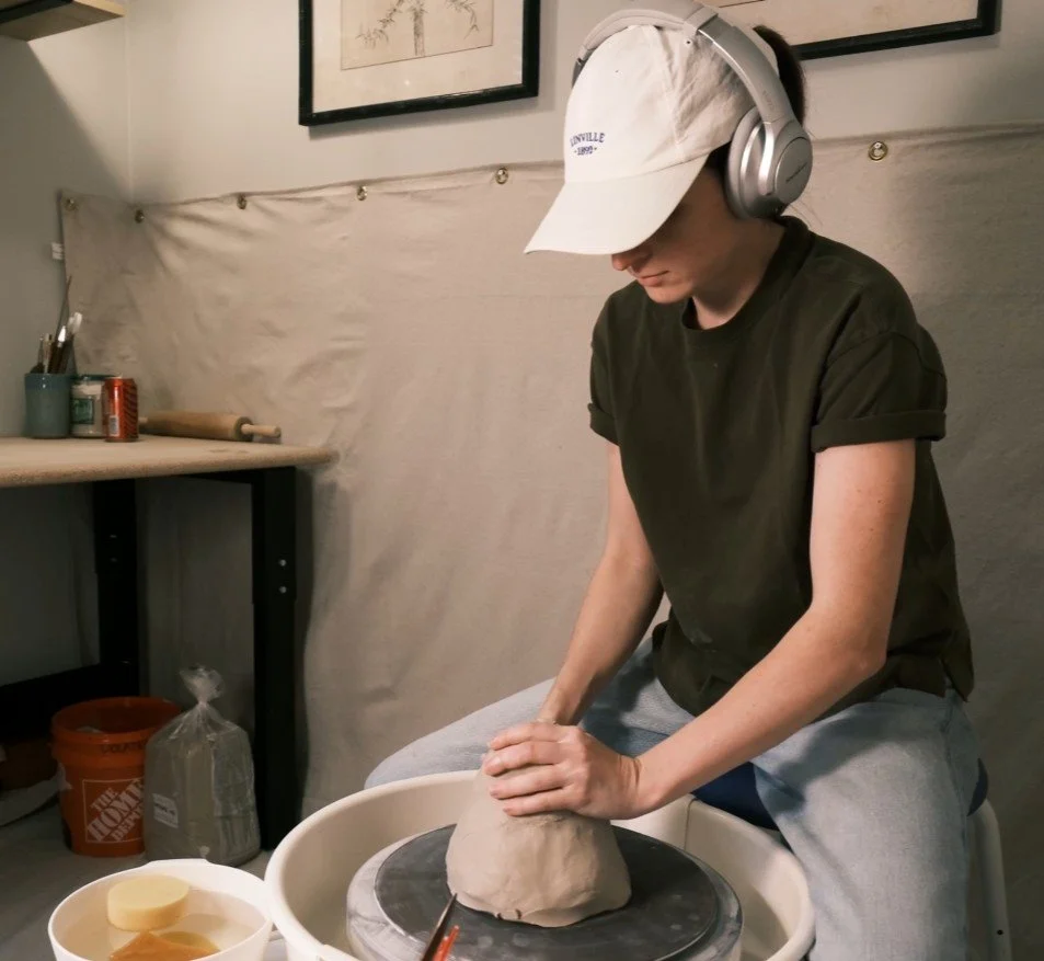 Artist, Ada Dolan, sitting and shaping clay on a pottery wheel.