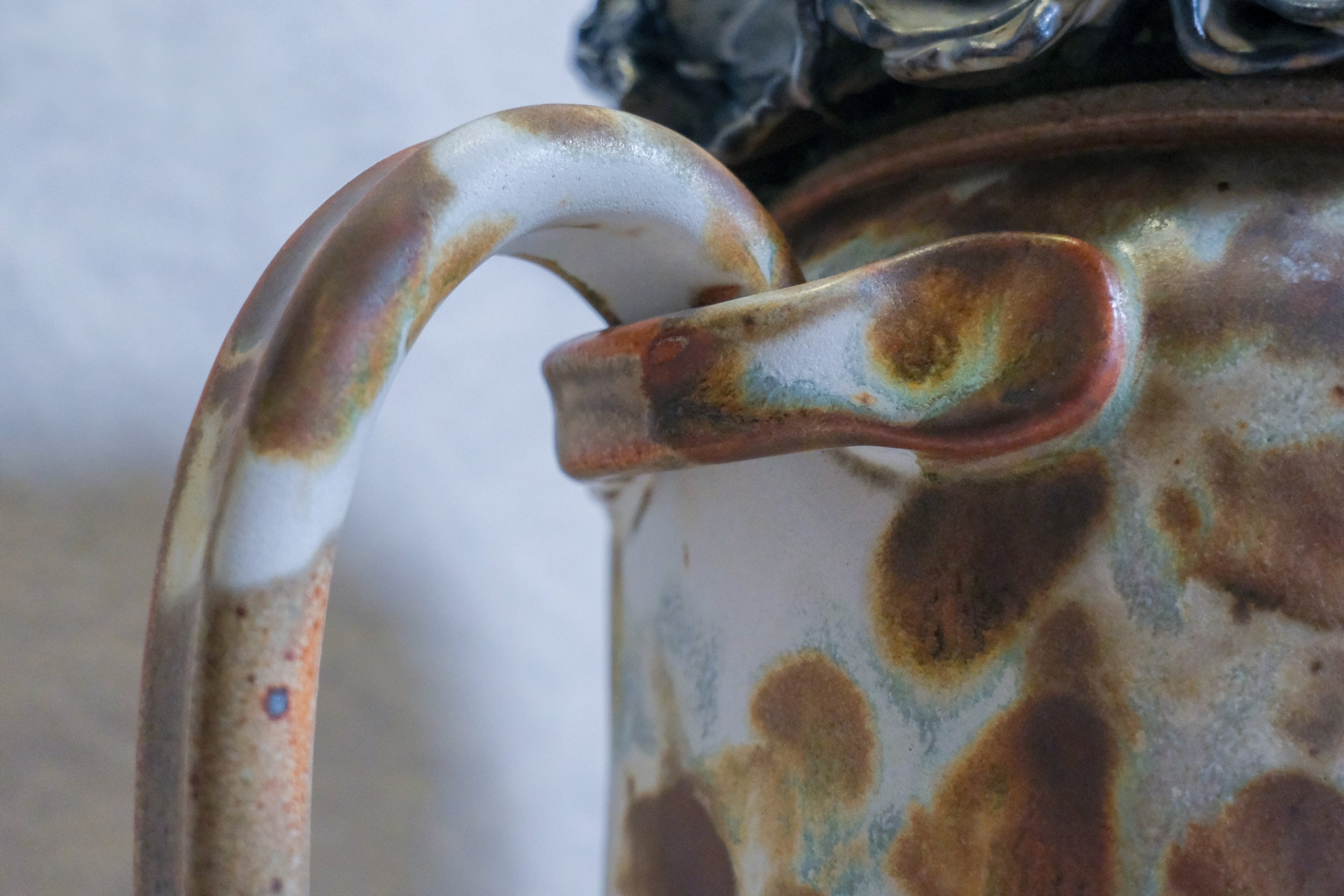 Close-up of a handle on a ceramic sculpture with blue and white hydrangea lid and a base with brown white, and blue abstract patterns.