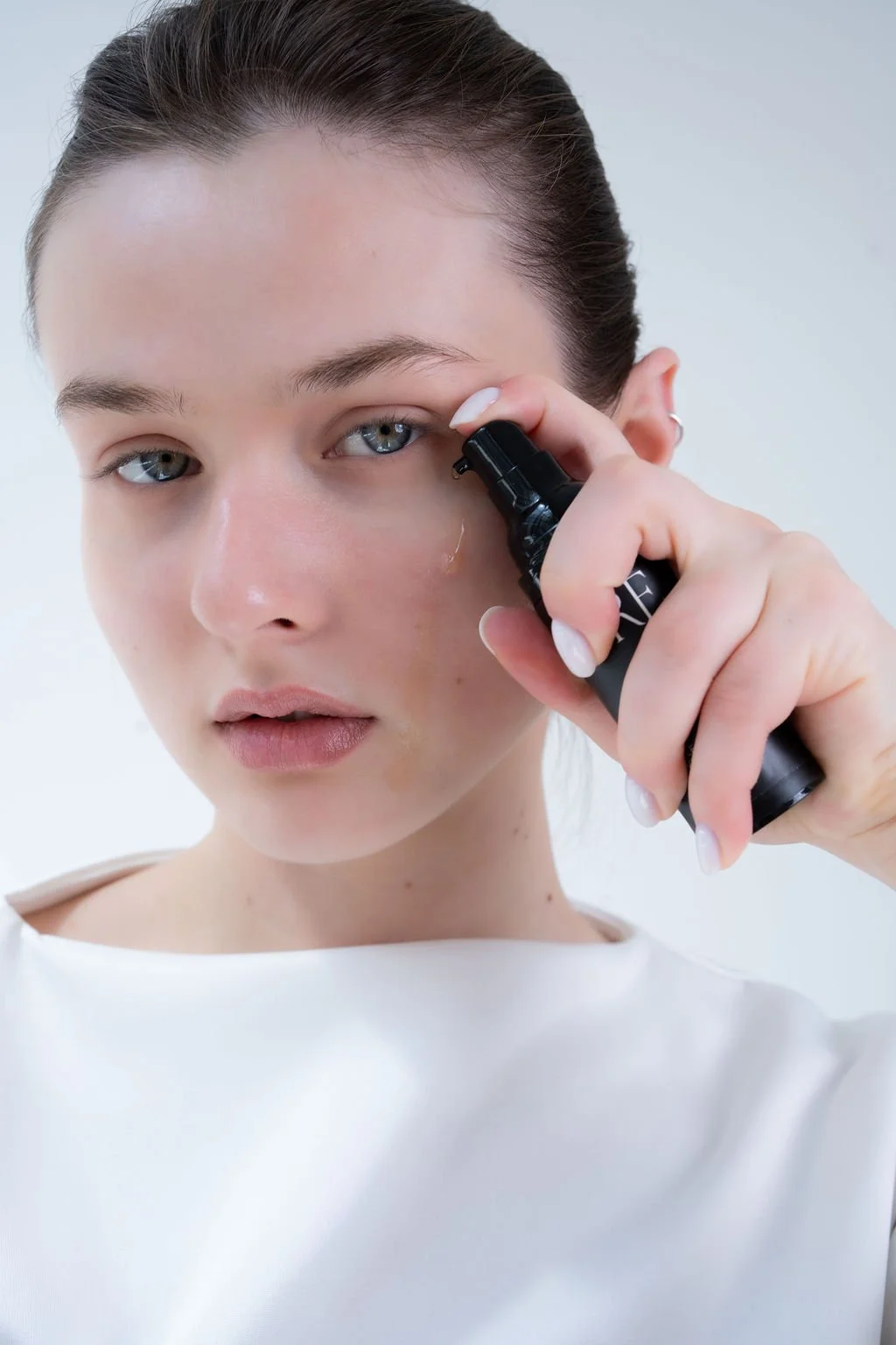 A young woman with blue eyes and dark hair pulled back, holding a skincare or facial massage device near her face.