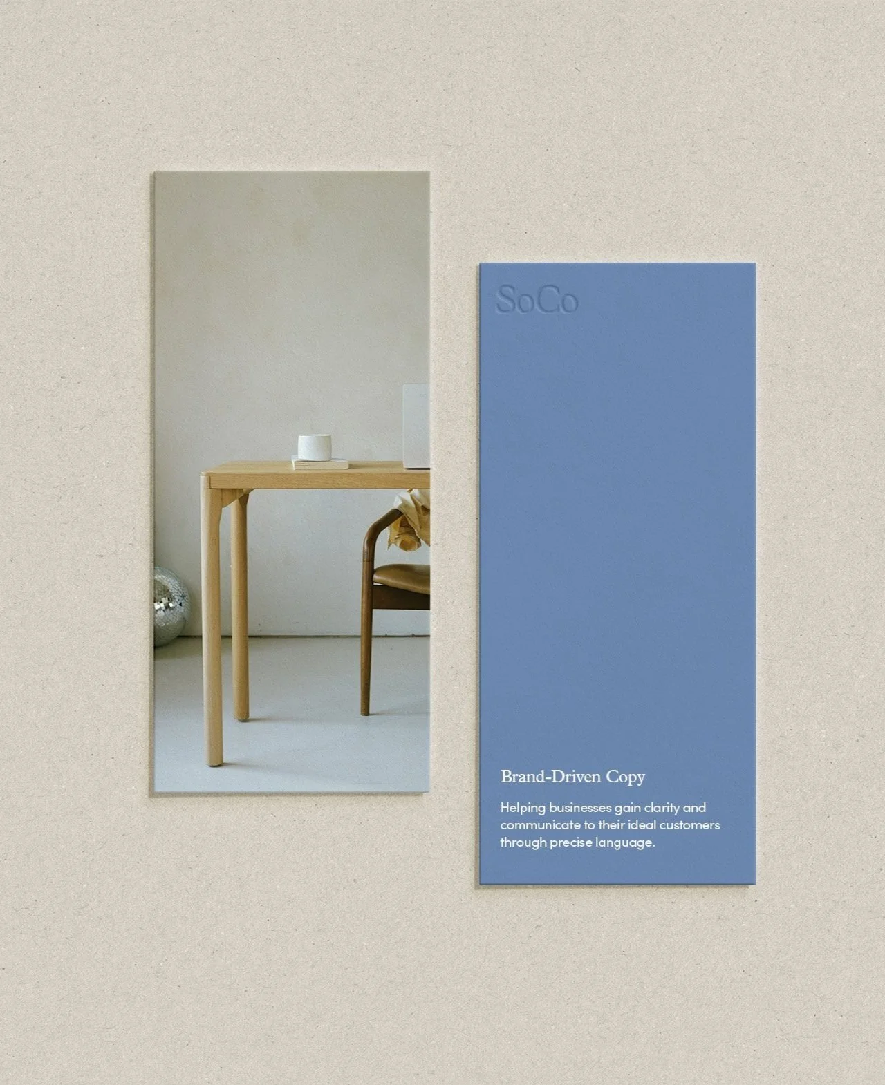 A mirror reflecting a light wood table with a white mug and a chair with a blanket, and a blue brochure titled 'Brand-Driven Copy' on a beige textured background.