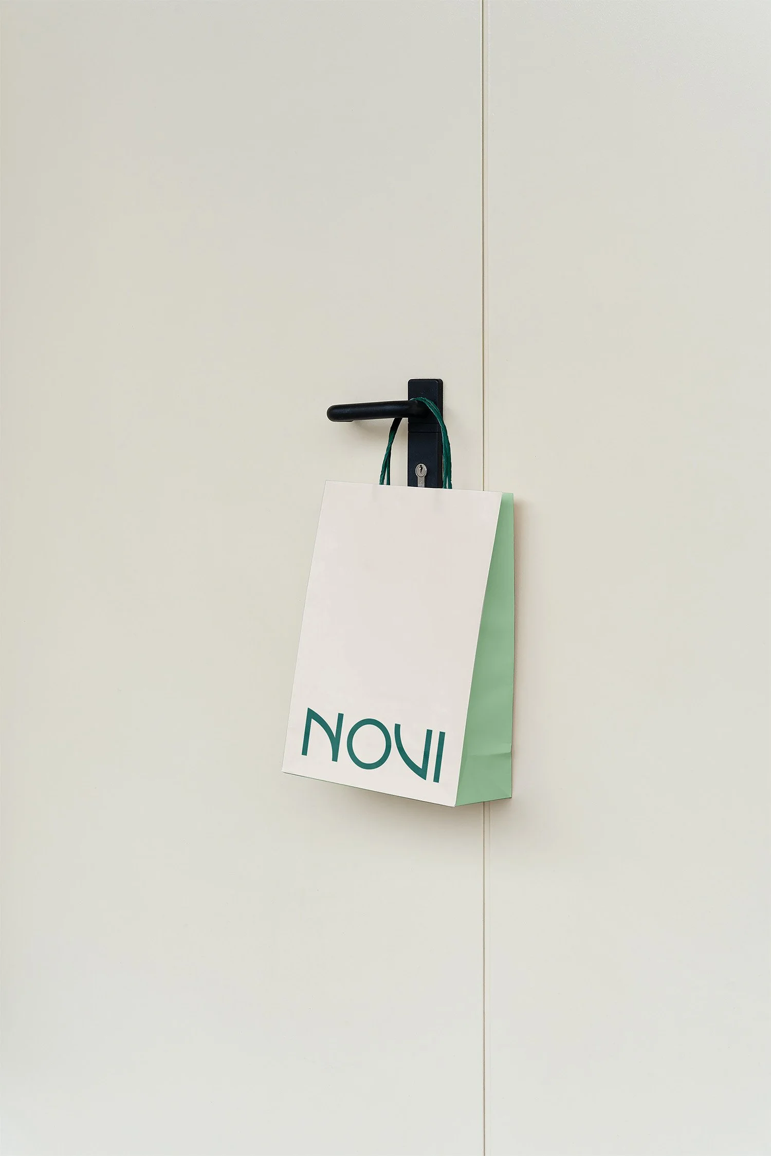 A white and green paper bag hanging on a black door handle with a green cord, with the word 'NOW' partially visible on the bag.