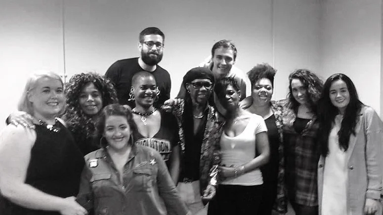 Group of ten diverse women and two men smiling and posing together in a room.
