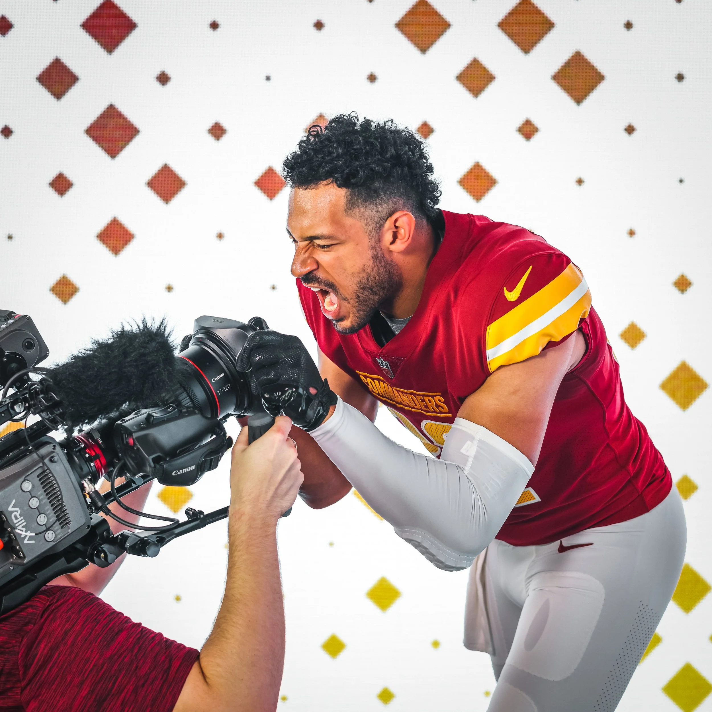 A football player in a red and yellow jersey is filming a scene with a professional camera, yelling with an intense expression on his face.