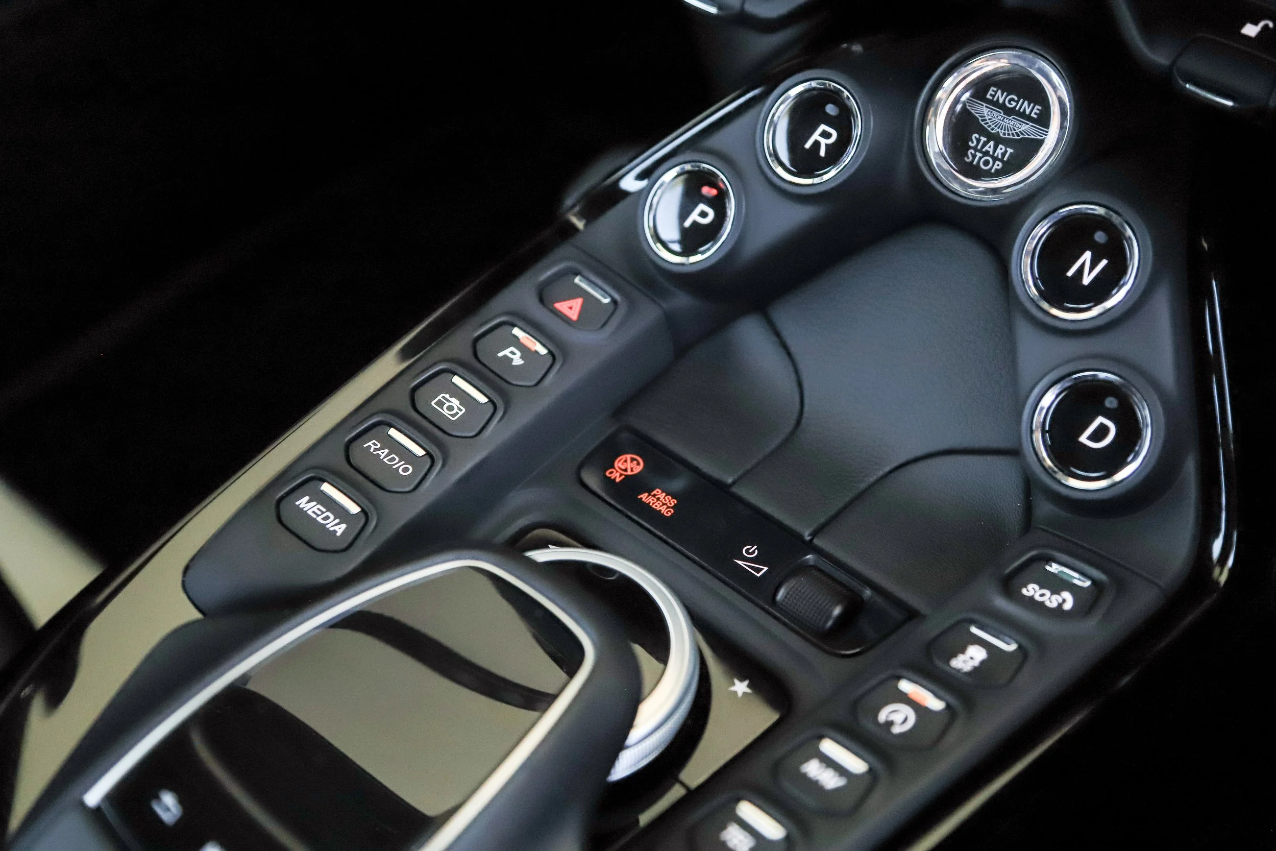 Close-up view of a luxury car's center console, featuring gear indicator lights for reverse, park, neutral, and drive, along with buttons for radio, media, hazard lights, and climate control.