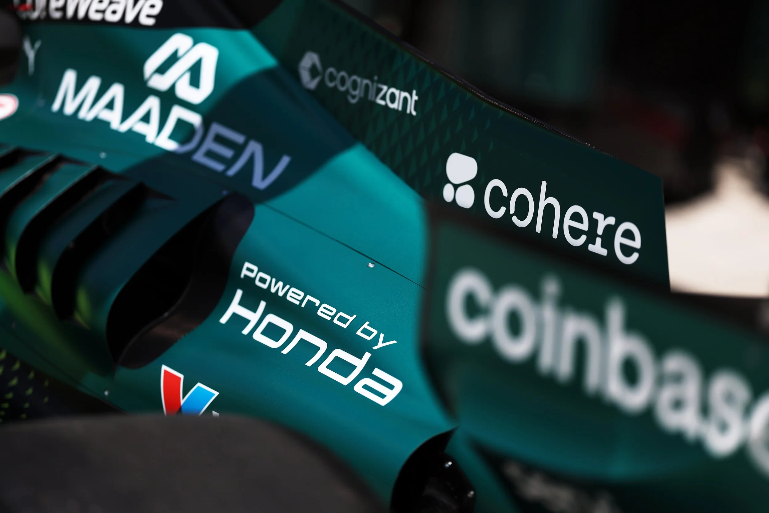 Close-up of a teal-colored racing bicycle frame with logos including Cofidis, BlueReef, and others, with carbon fiber fork blades visible.