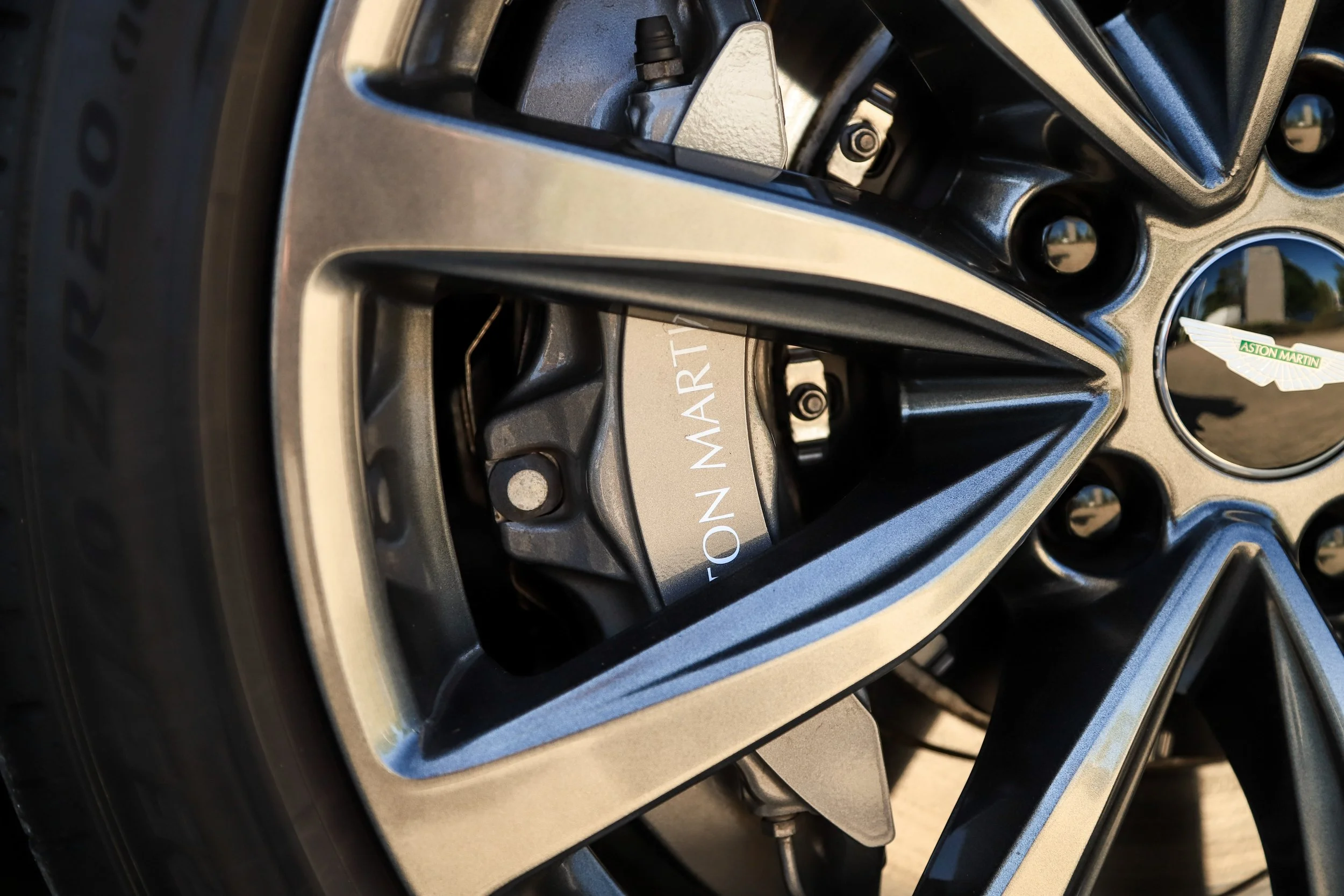 Close-up of an Aston Martin car wheel with a visible brake caliper and the Aston Martin logo.