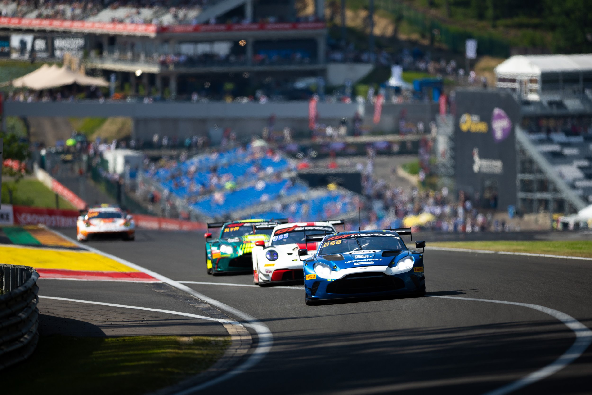 Race cars competing on a track during a motorsport event, with spectators and structures in the background.