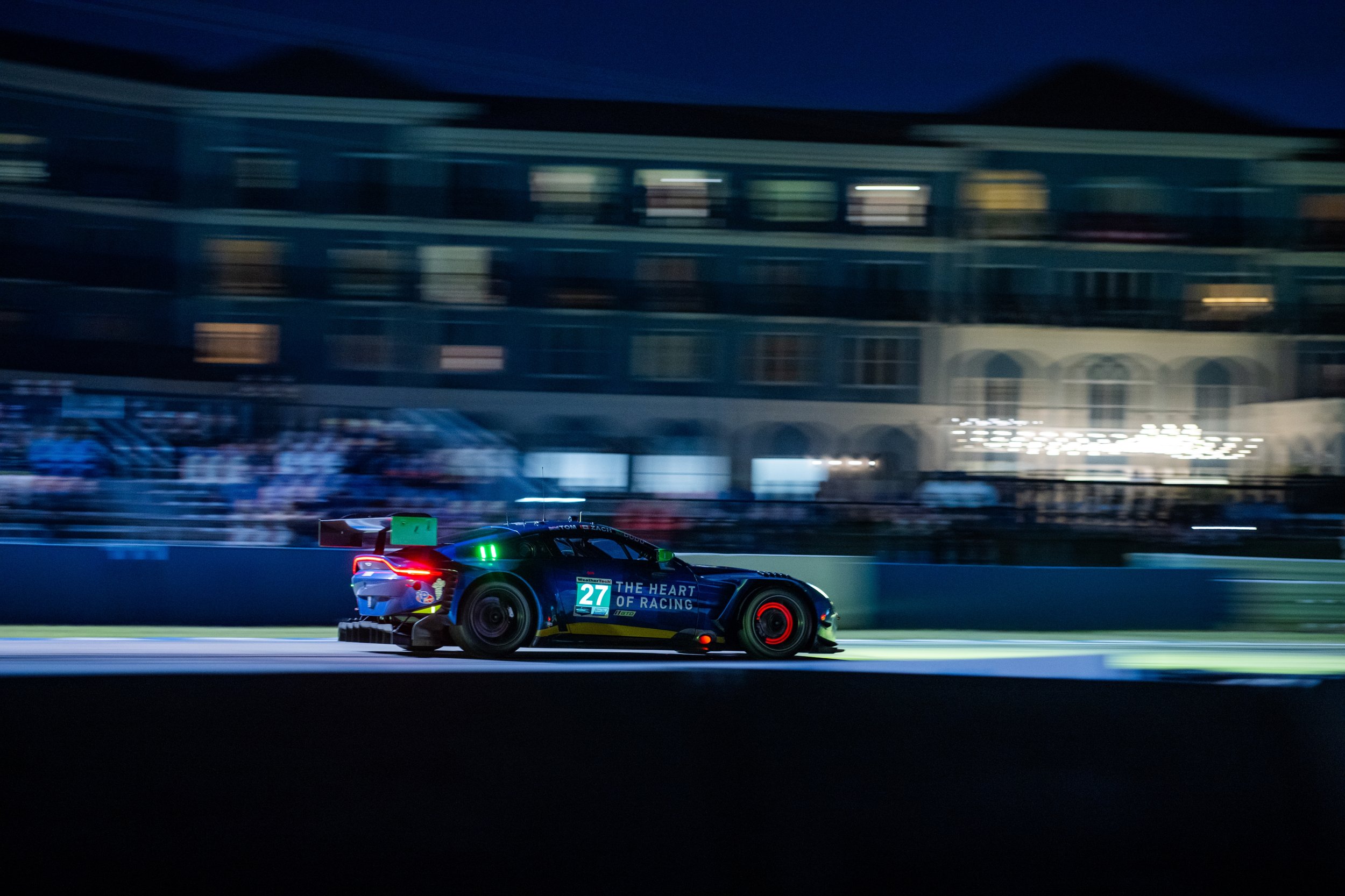 Race car with the number 27 and the words 'The Heart of Racing' racing on a track at night.