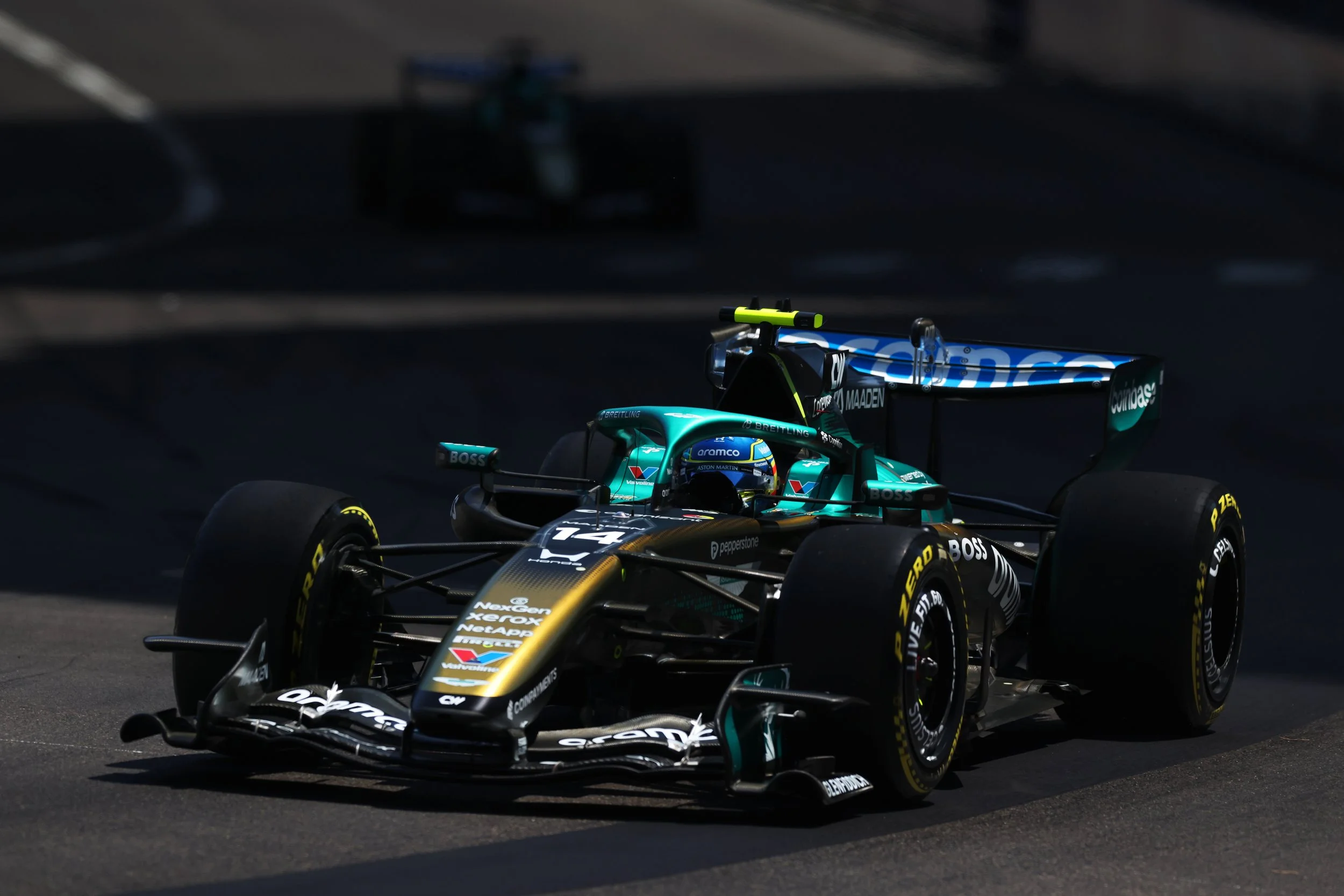 The special livery of the AMR26 Aston Martin Racing Formula 1 race car with sponsorship decals, speeding on a dark asphalt track at Monaco.