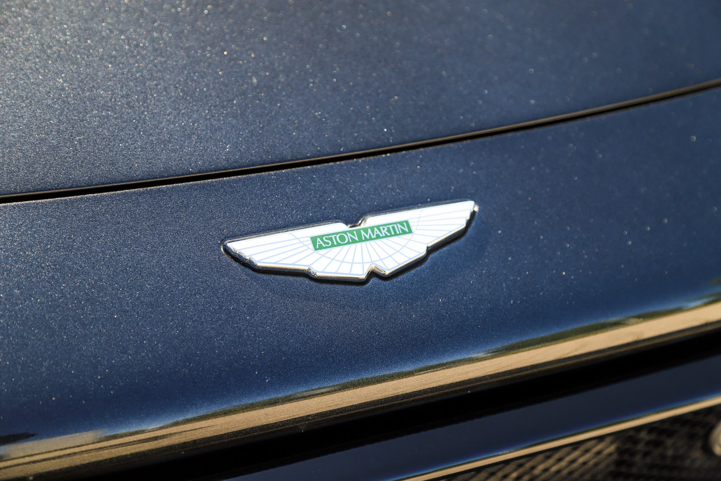 Close-up of an Aston Martin car emblem on a dark blue metallic car surface.