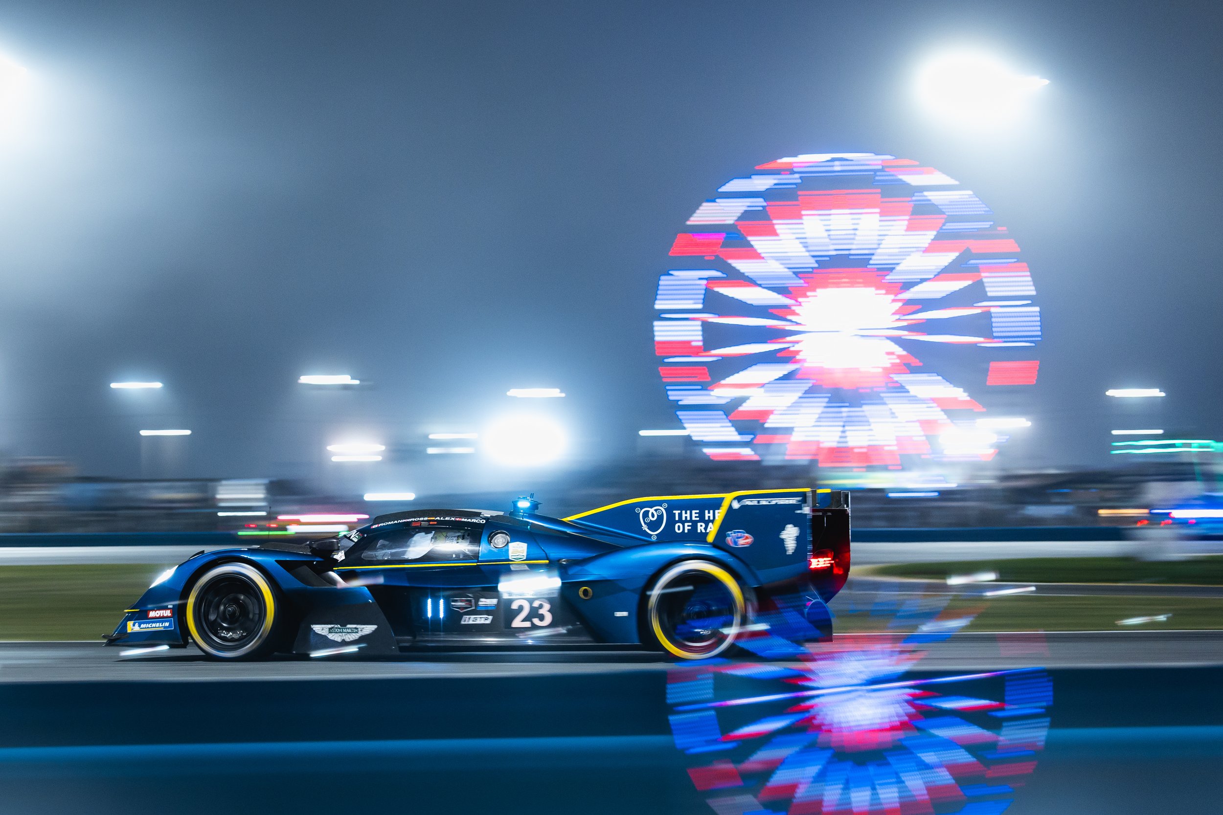 A racing car on a track at night, with bright colorful lights, including a large illuminated number eight in the background.