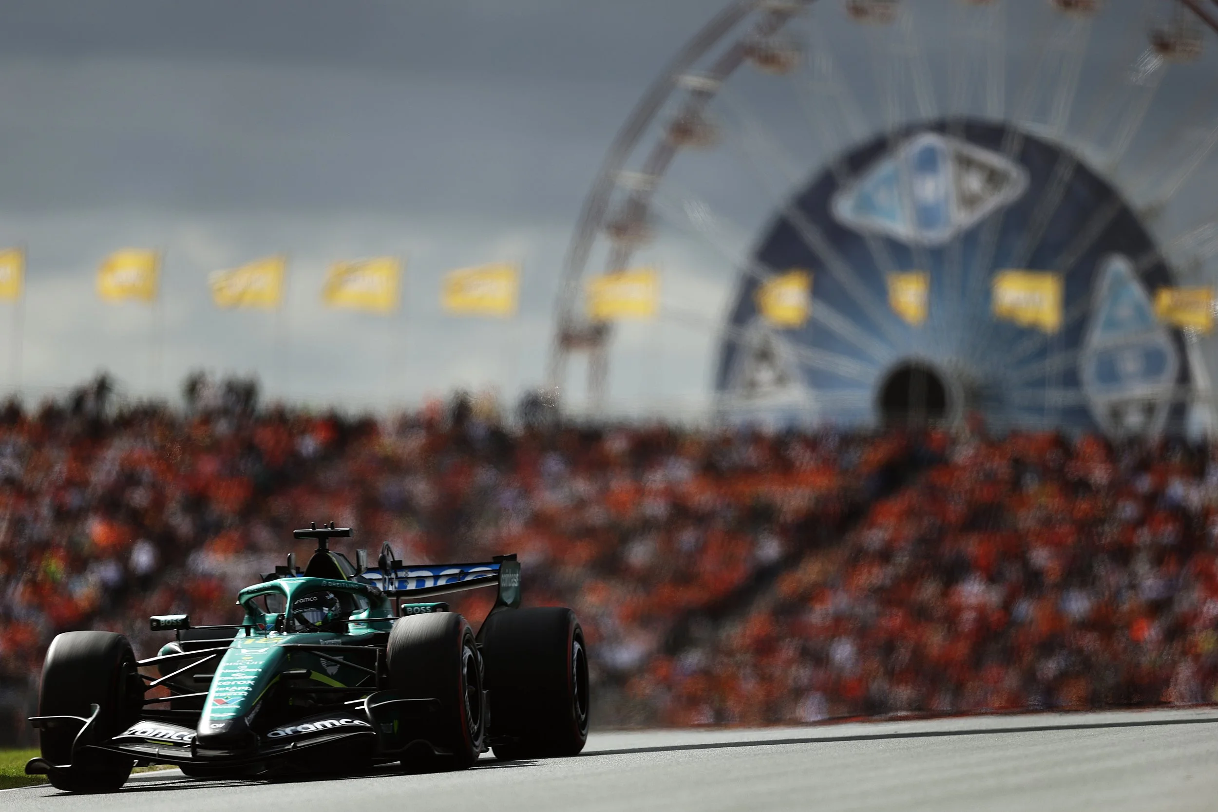 A Formula 1 race car on a track with a large Ferris wheel in the background and a crowd of spectators.