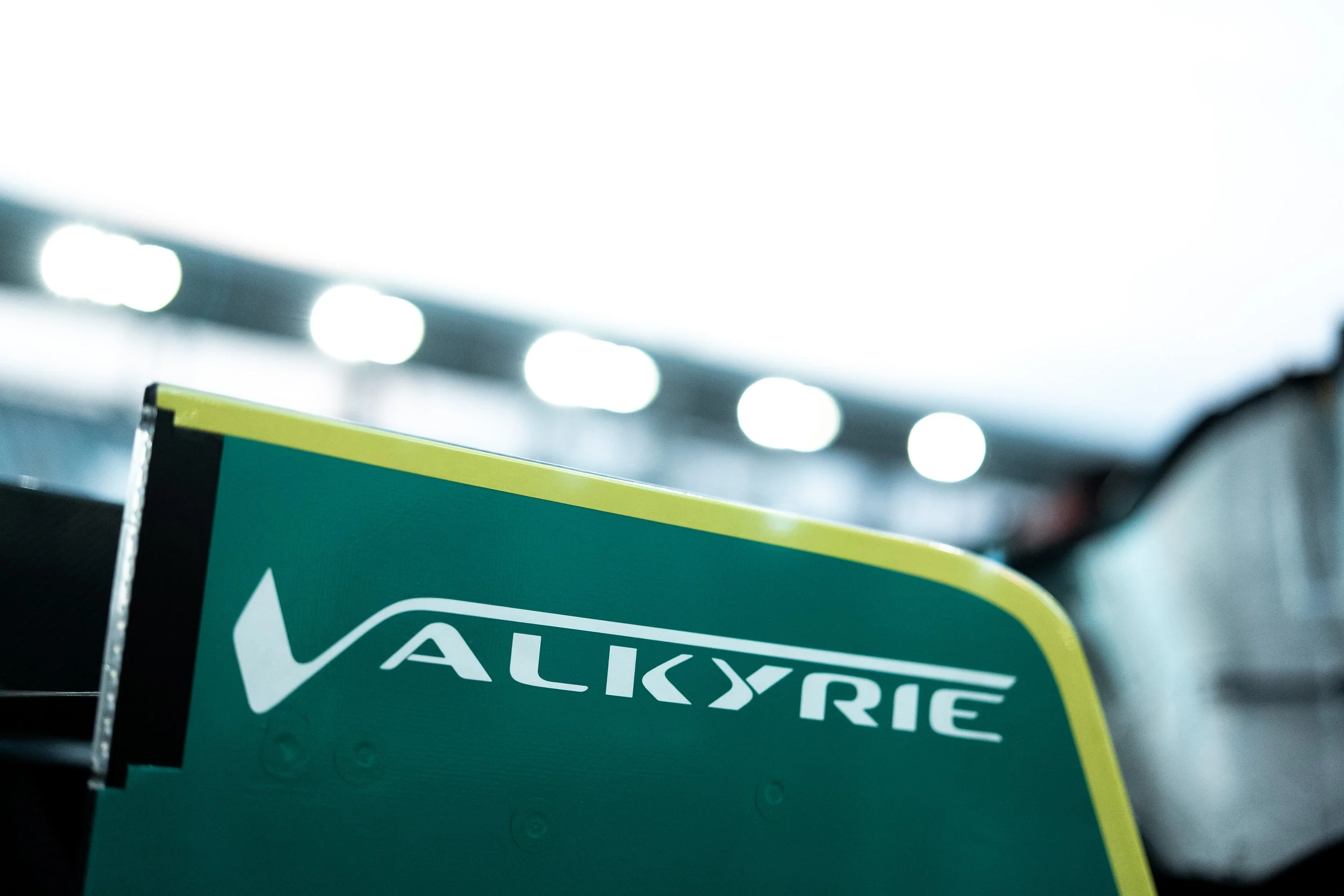 Close-up image of a green Valvoline engine oil container with a yellow stripe, partially visible in front of a blurred background of bright lights, possibly in a store or garage.