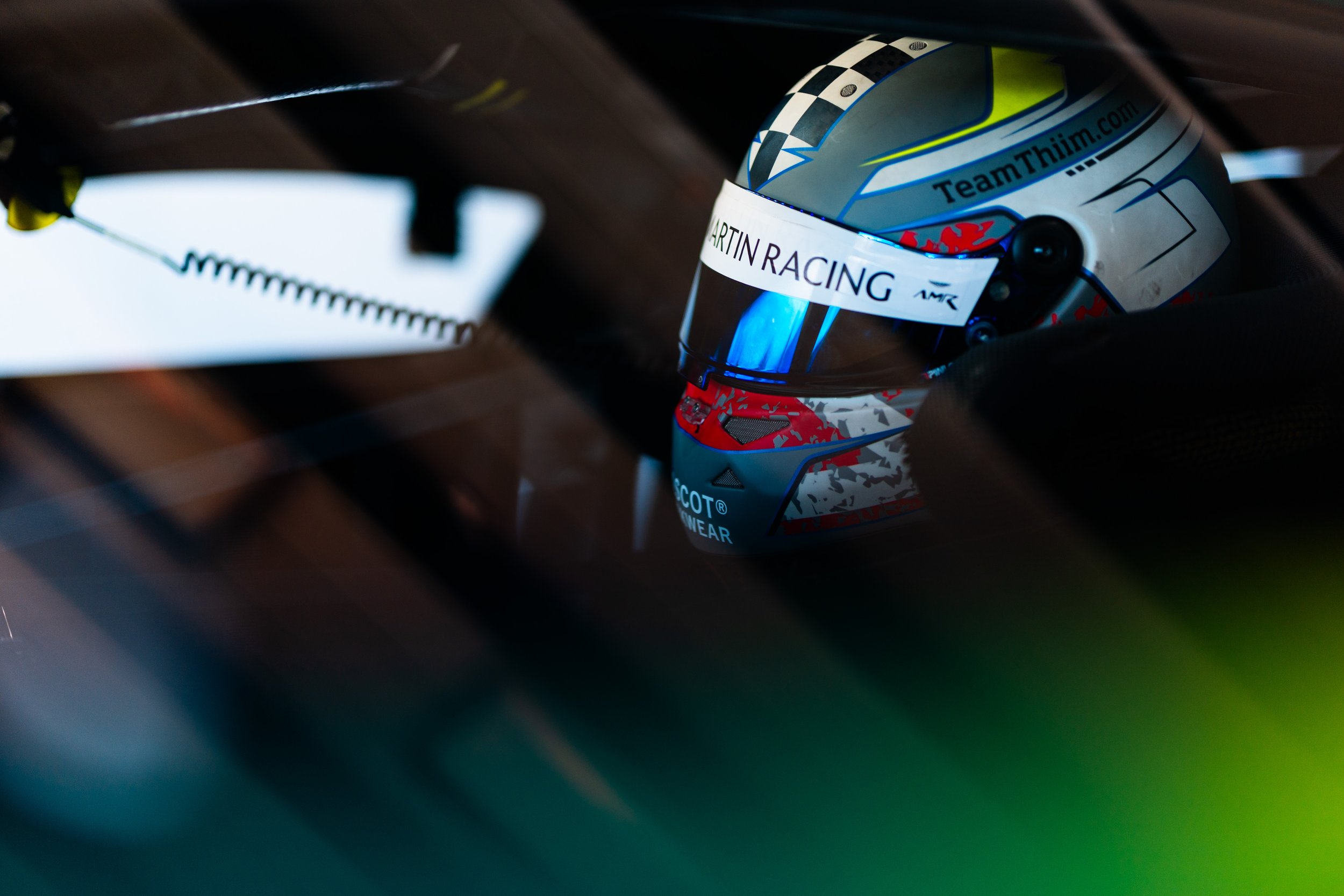 Close-up of a racing helmet with dark goggles, featuring the words 'Team Thiiim' and 'Start in Racing' on the front, inside a car with a checkered flag pattern on the top.