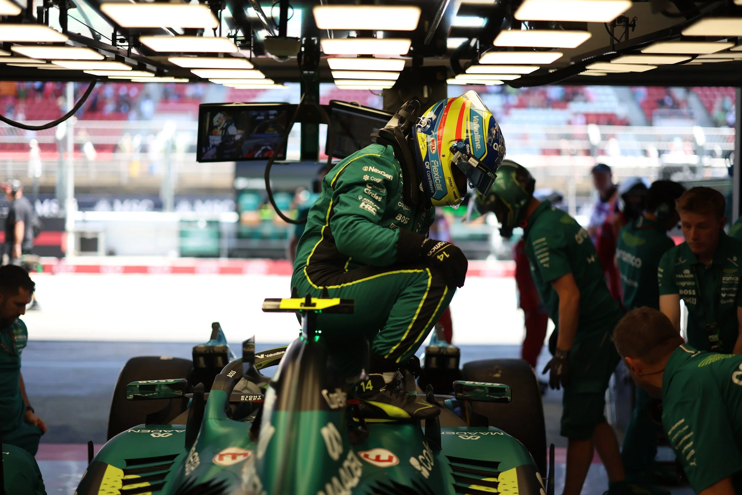 Fernando Alonso getting into his AMR26 at the Barcelona Grand Prix 2026, with team members around him.
