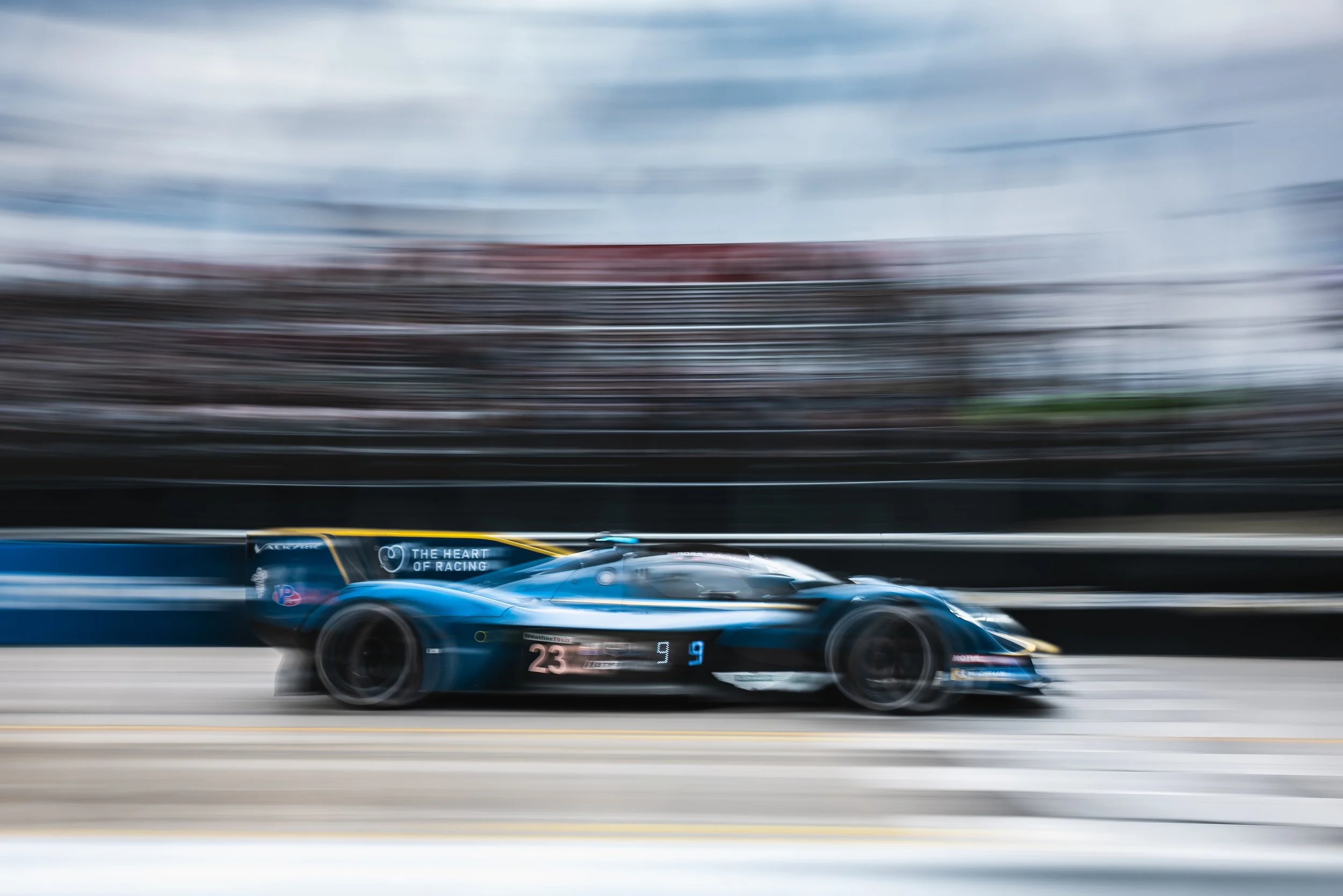 An Aston Martin Valkyrie race car speeding on a track with motion blur in the background, with the number 23 on the front.