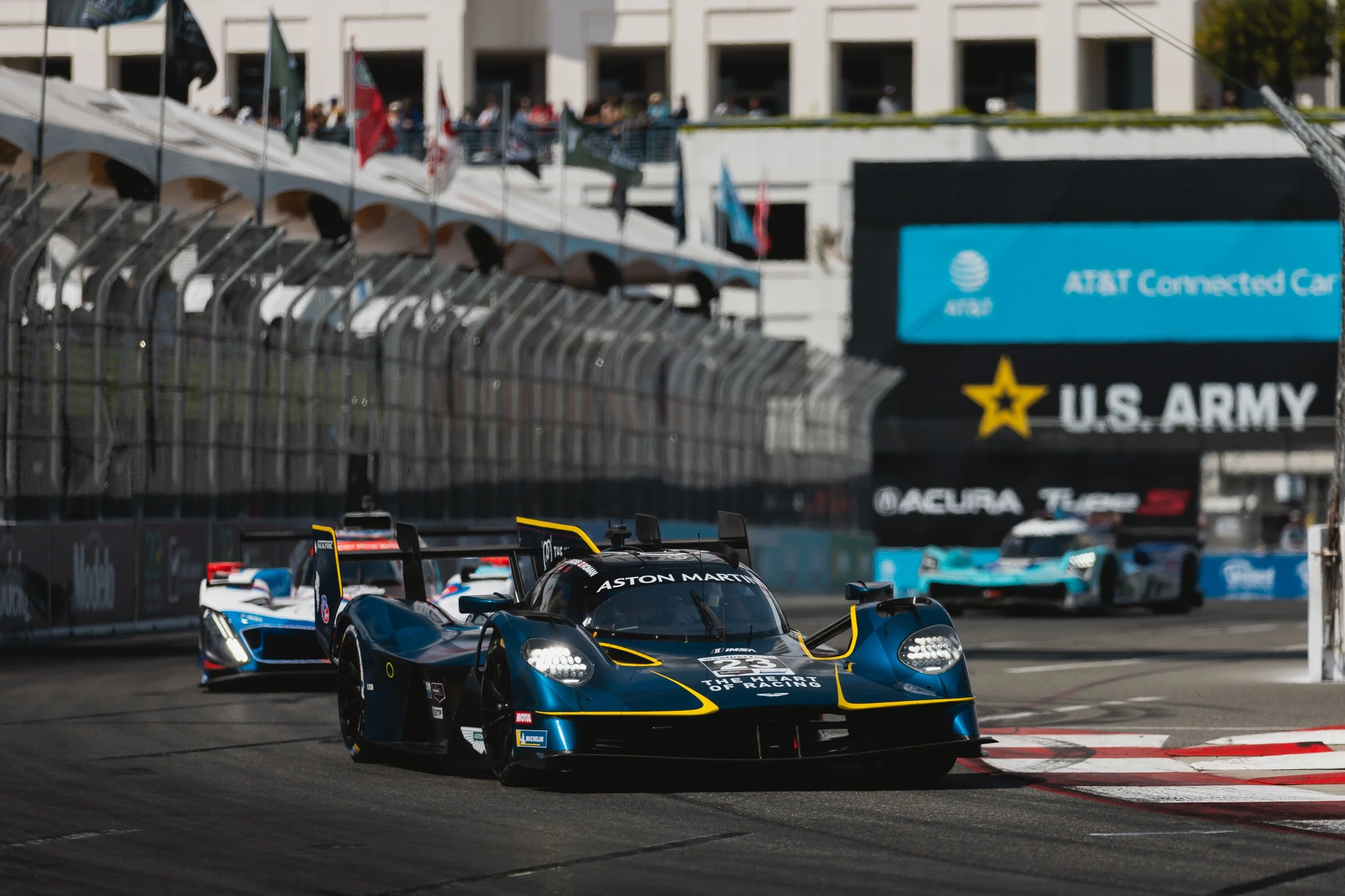 An Aston Martin Valkyrie driving on a racing track during a motorsport event, with spectators and flags visible in the background.