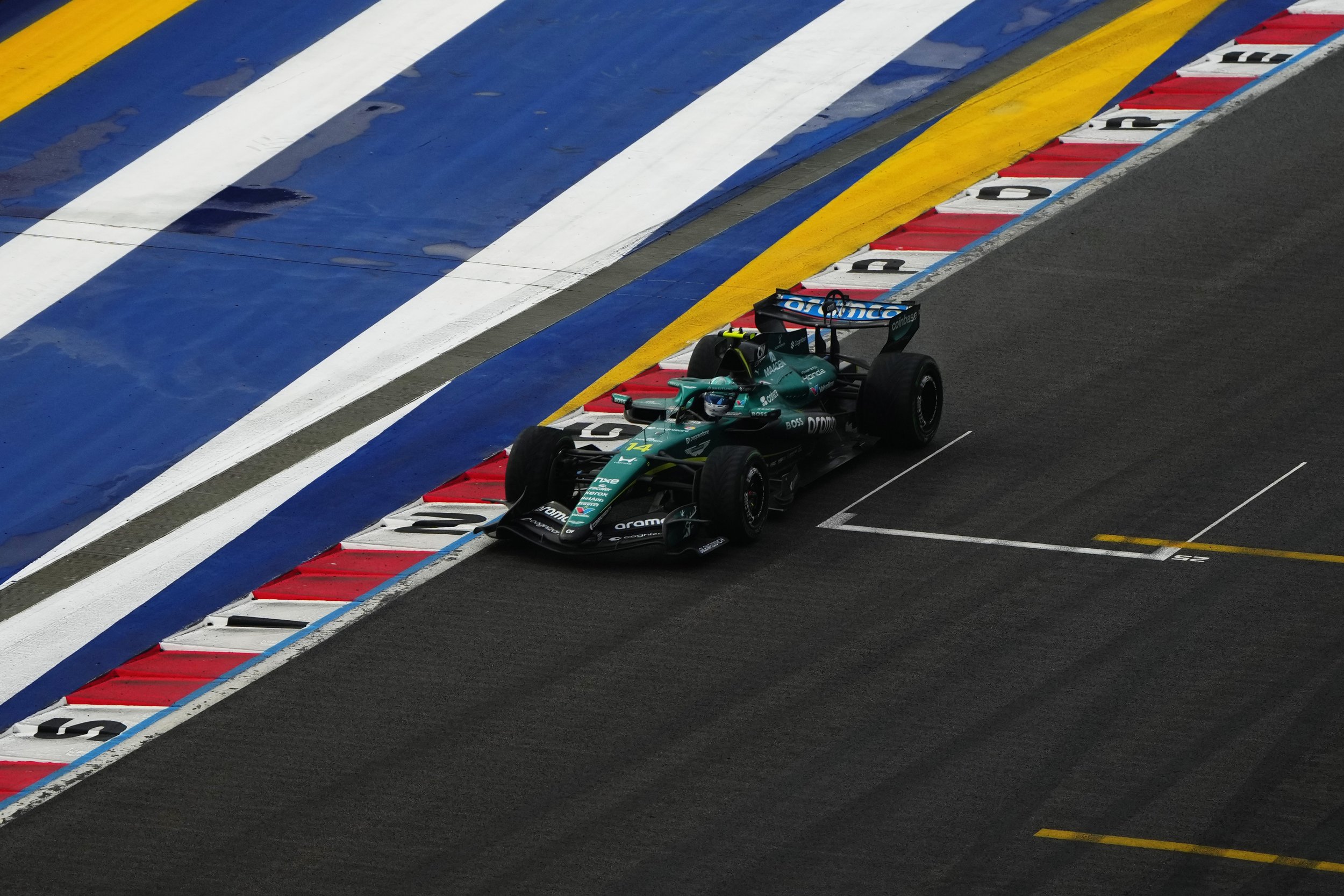 A race car on a racing track near the pit lane with colorful painted curbs including yellow, white, blue, and red sections.