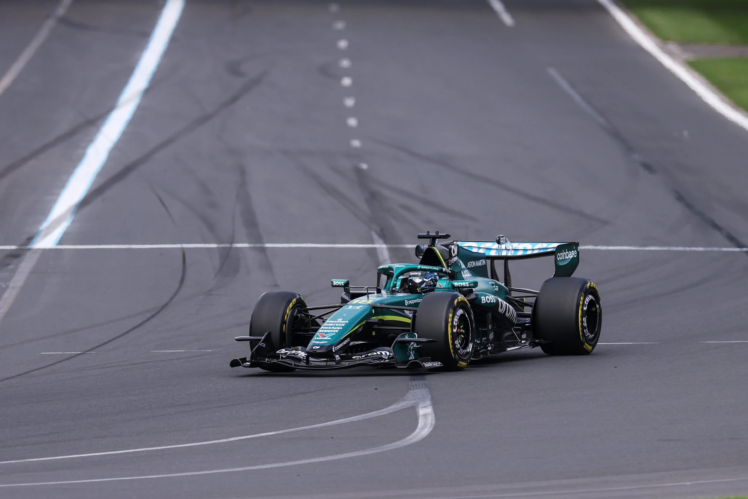 An Aston Martin Formula 1 race car on a race track, with a blue and black livery, branded with various sponsor logos including Coinbase and Aston Martin.