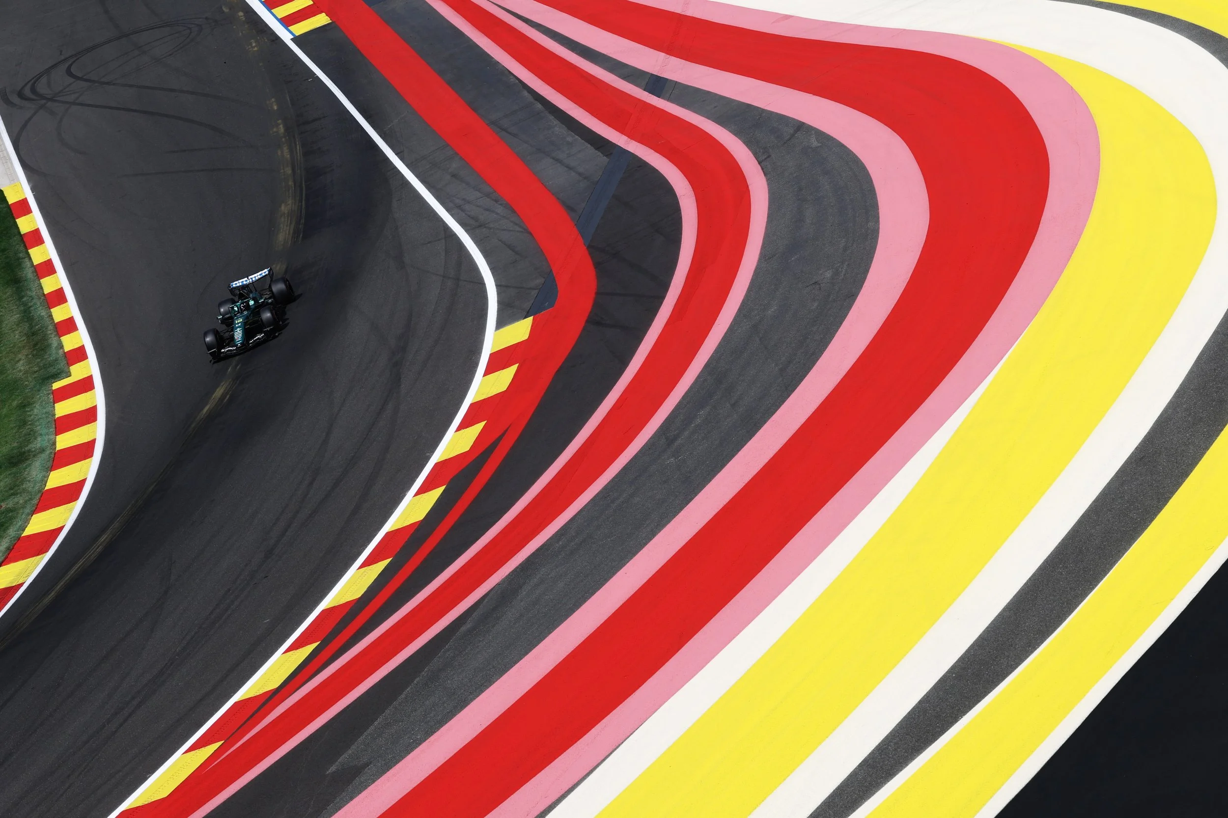 A race car on a brightly colored, winding race track with multiple red, pink, and yellow striped sections and a black section with tire skid marks.