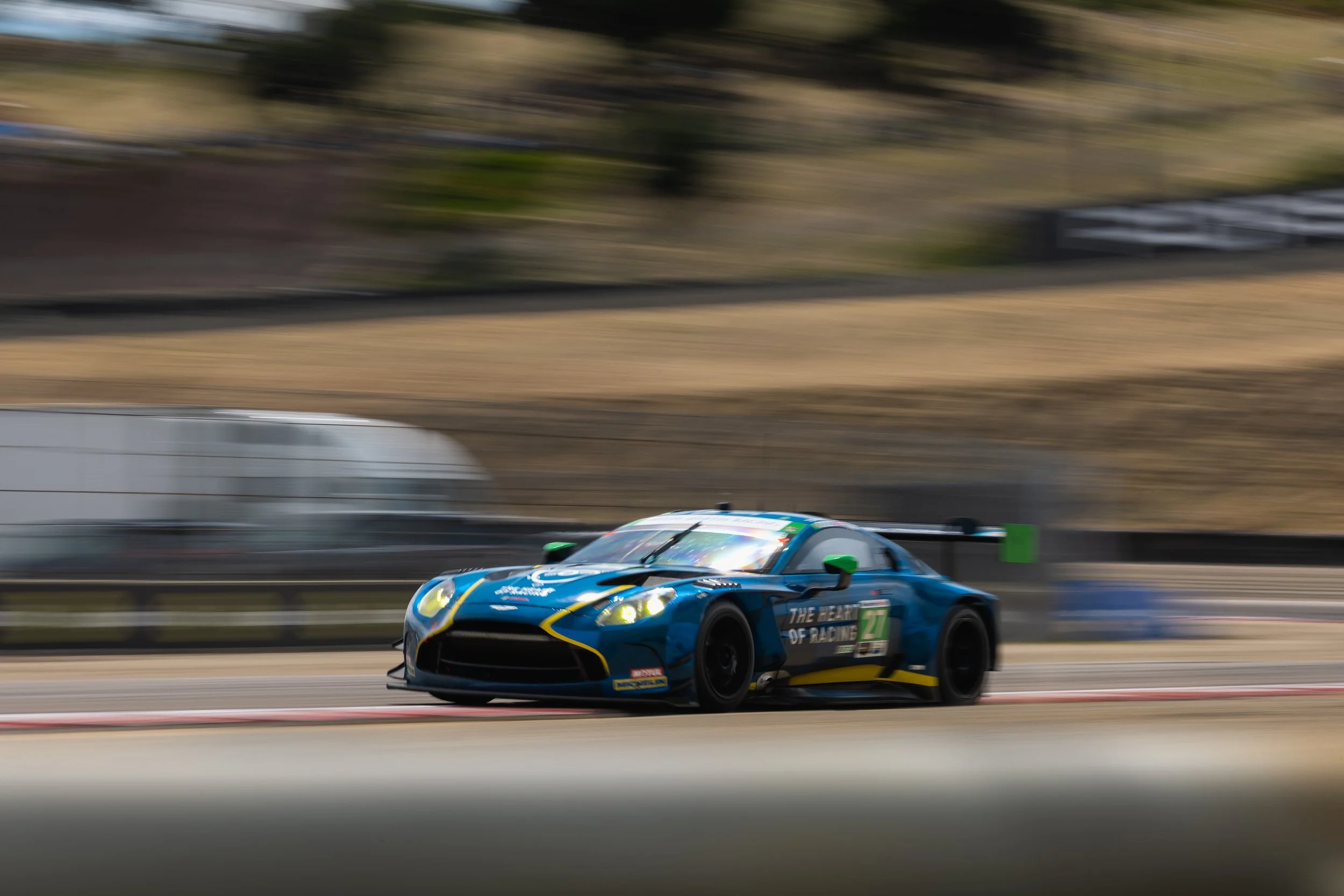 A blue race car with yellow and green accents speeding on a racetrack, with a blurred background indicating motion.