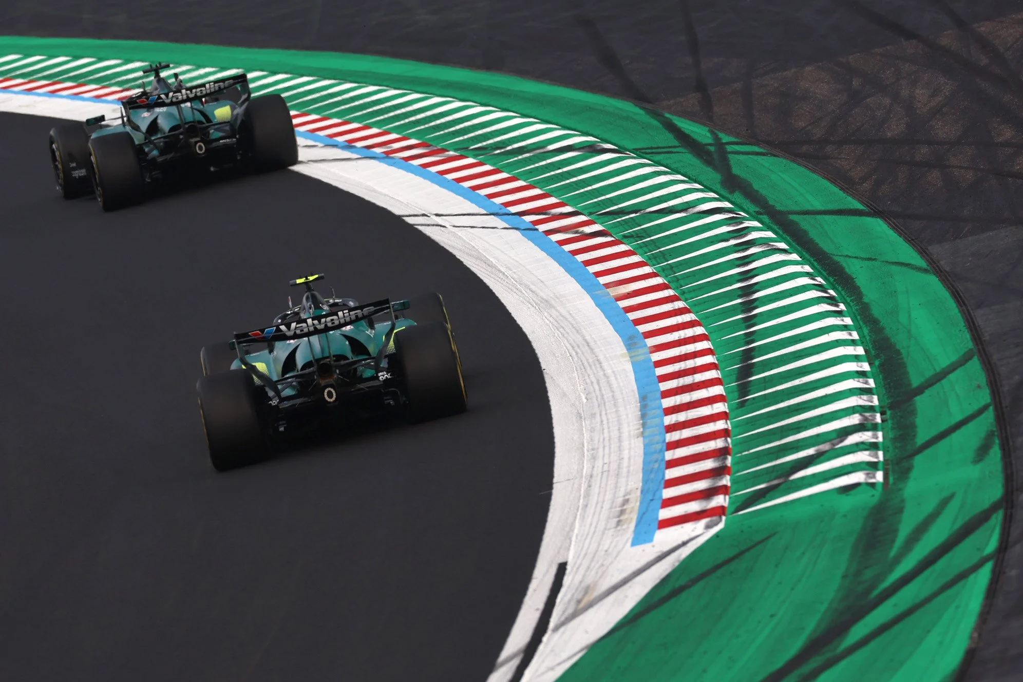 Two race cars on a racetrack with colorful curbing, including green, red, white, and blue stripes, during a racing event.