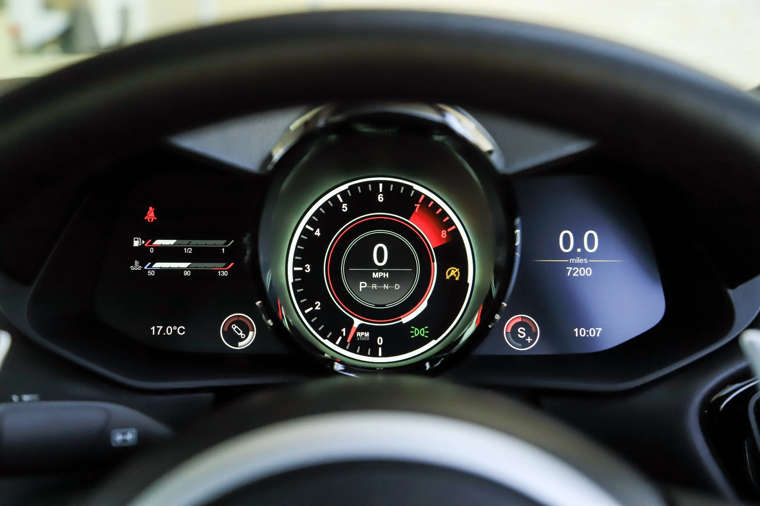 Digital car dashboard displaying speed of 0 MPH, 0.0 miles traveled, 7200 miles total, with engine RPM at zero, and warning lights including seatbelt, tire pressure, and engine check. Temperature shown as 17.0°C, and time as 10:07.