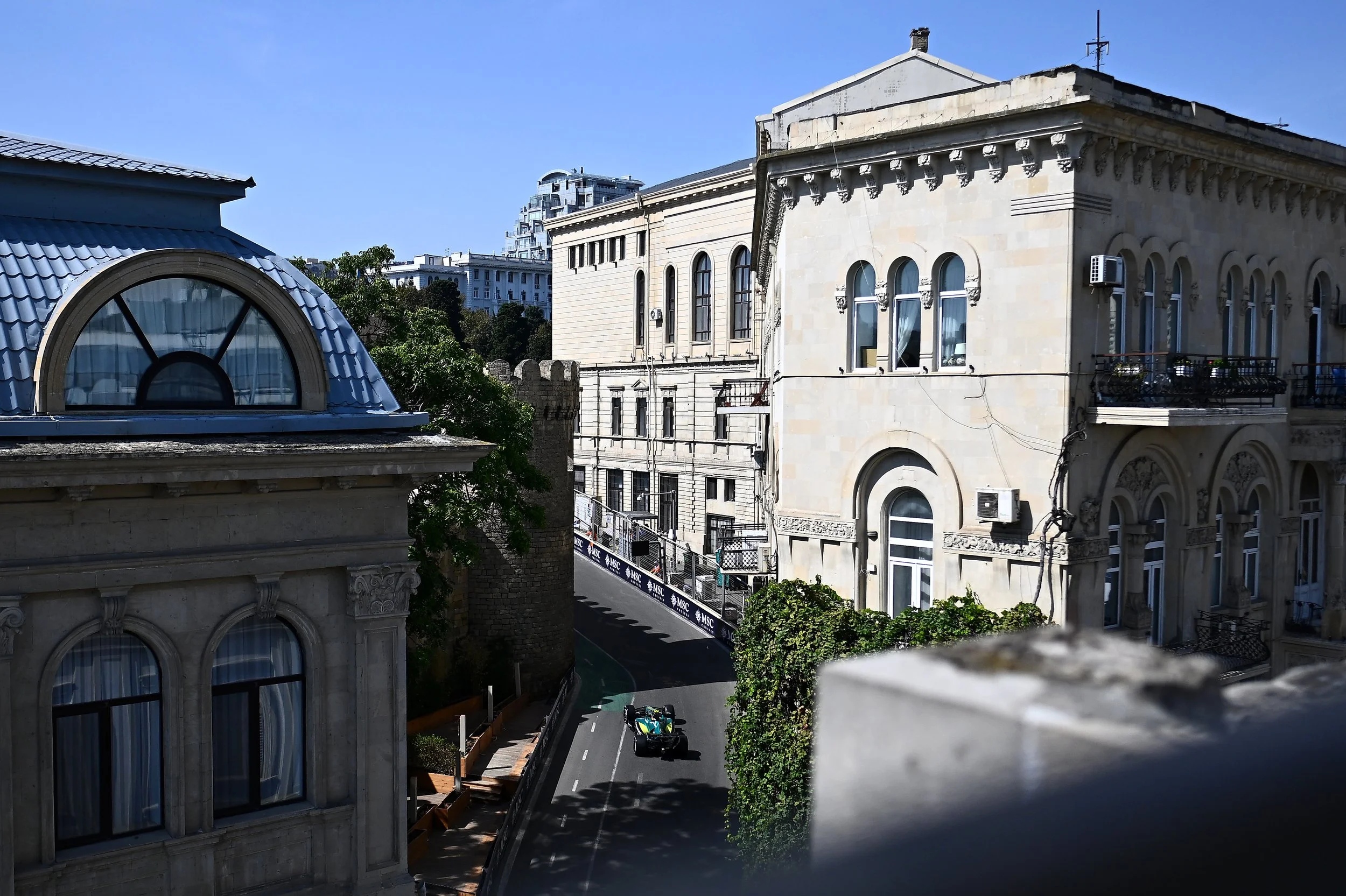 View of buildings, including a rooftop with a blue tiled dome, and trees lining the street below with two green and black golf carts on the road under a clear blue sky.